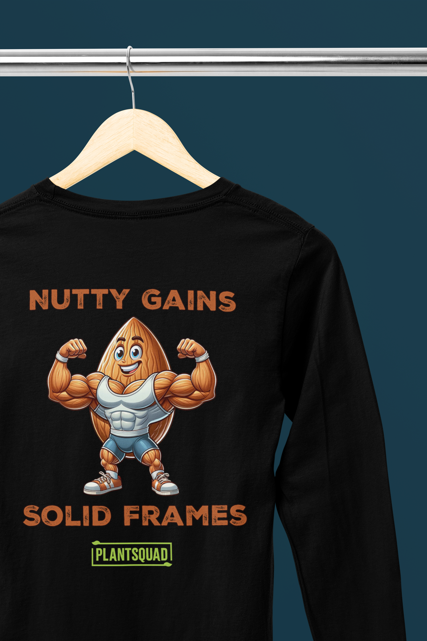 The Plantsquad Almond "Nutty Gains Solid Frames" - Unisex Long Sleeve T-Shirt features a muscly almond cartoon flexing its biceps. Above it are the words "NUTTY GAINS," and below is "SOLID FRAMES." At the bottom, there is a green rectangle with the word "PLANTSQUAD" in yellow letters, perfect for those embracing a vegan fitness lifestyle.