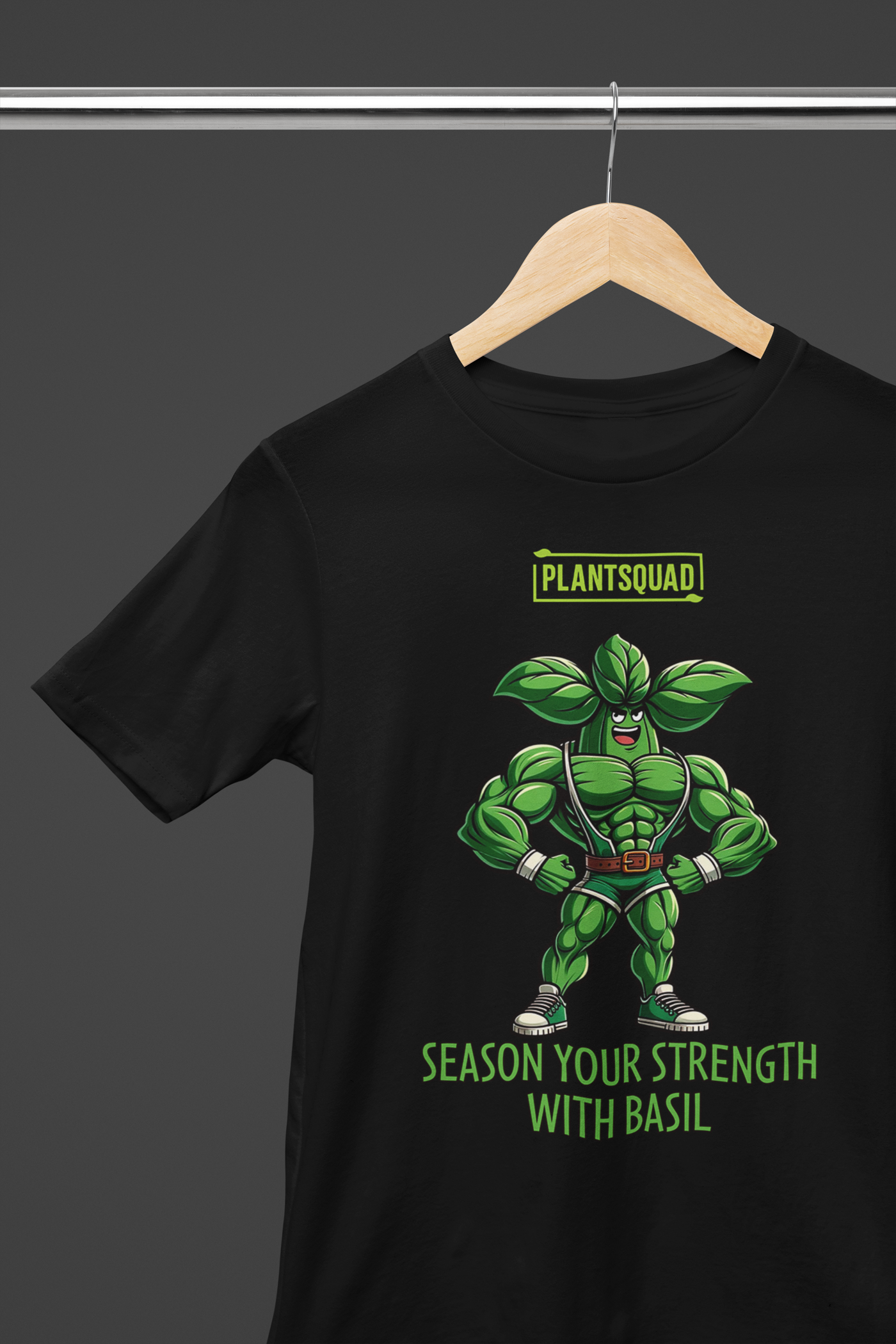 A black t-shirt features a muscular green basil superhero with leafy arms and head, wearing a cape and gloves. Above the character is the bold text "PLANTSQUAD," and below it reads "SEASON YOUR STRENGTH WITH BASIL." Embrace your inner plantsquad hero with the Plantsquad Basil "Season Your Strength With Basil" - Unisex T-Shirt!