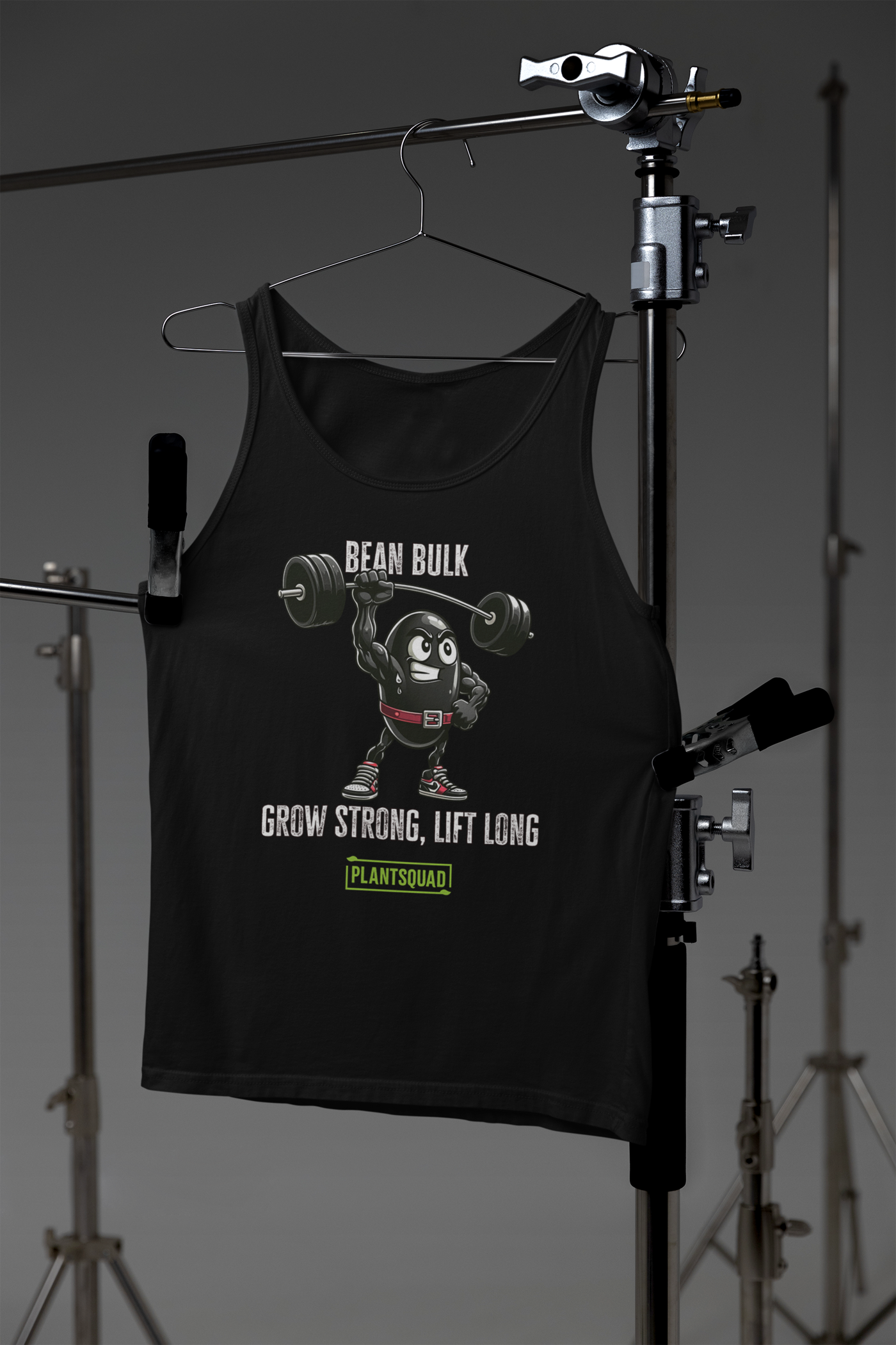 The Plantsquad Black Bean "Bean Bulk Grow Strong Lift Long" - Unisex Tank Top features a cartoon bean character lifting a barbell with the text "BEAN BULK" above and "GROW STRONG, LIFT LONG" below. Perfect for gym enthusiasts embracing a plant-based lifestyle, it has the logo "PLANTSQUAD" in green at the bottom. The bean wears red gloves, a red belt, and red shoes.