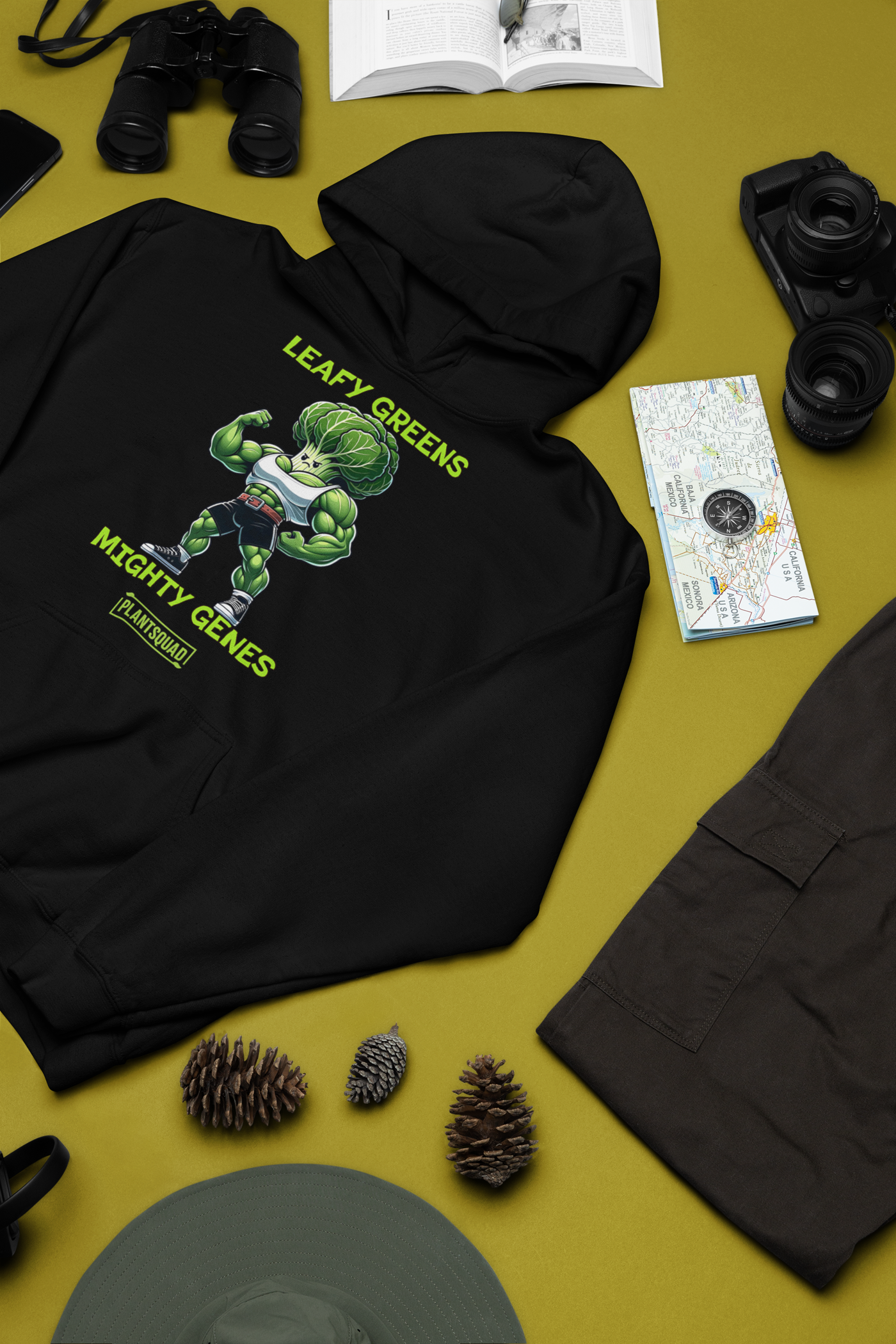 A black Plantsquad Cabbage "Leafy Greens Mighty Genes" - Unisex Hoodie featuring a graphic of a muscular cabbage cartoon with a lettuce head, wearing sunglasses and flexing its arms. The cozy fabric ensures comfort while the text above reads "LEAFY GREENS," below reads "MIGHTY GENES," and "PLANT SQUAD" displayed in a rectangular box. Perfect for championing the vegan lifestyle.