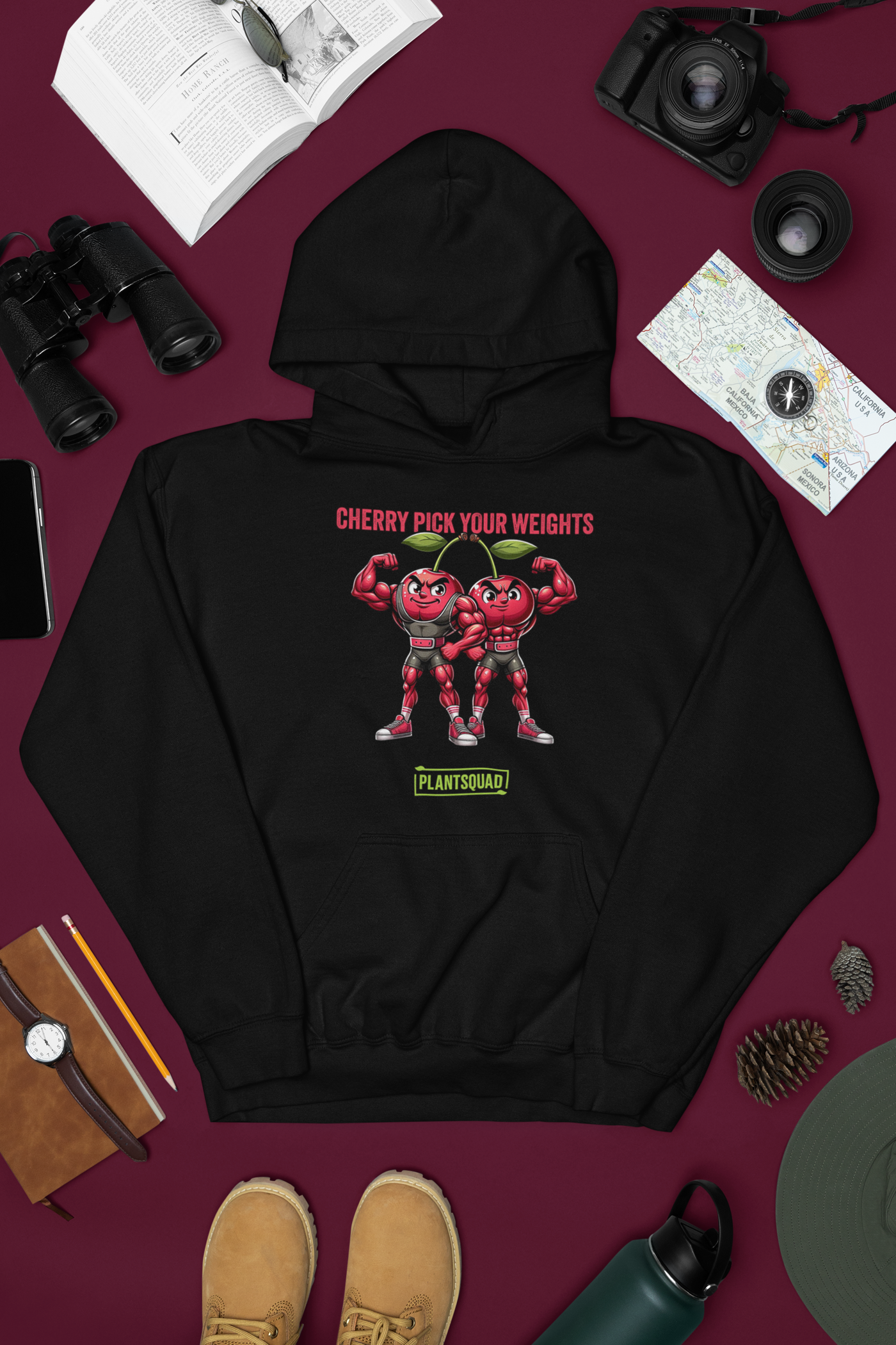 The Plantsquad Cherries "Cherry Pick Your Weights" - Unisex Hoodie features a graphic design on the front. The design includes two anthropomorphized cherries with muscular arms, flexing their muscles. Above them, the text reads "CHERRY PICK YOUR WEIGHTS." Below the cherries, there is a green "PLANTSQUAD" logo that celebrates the vegan lifestyle.