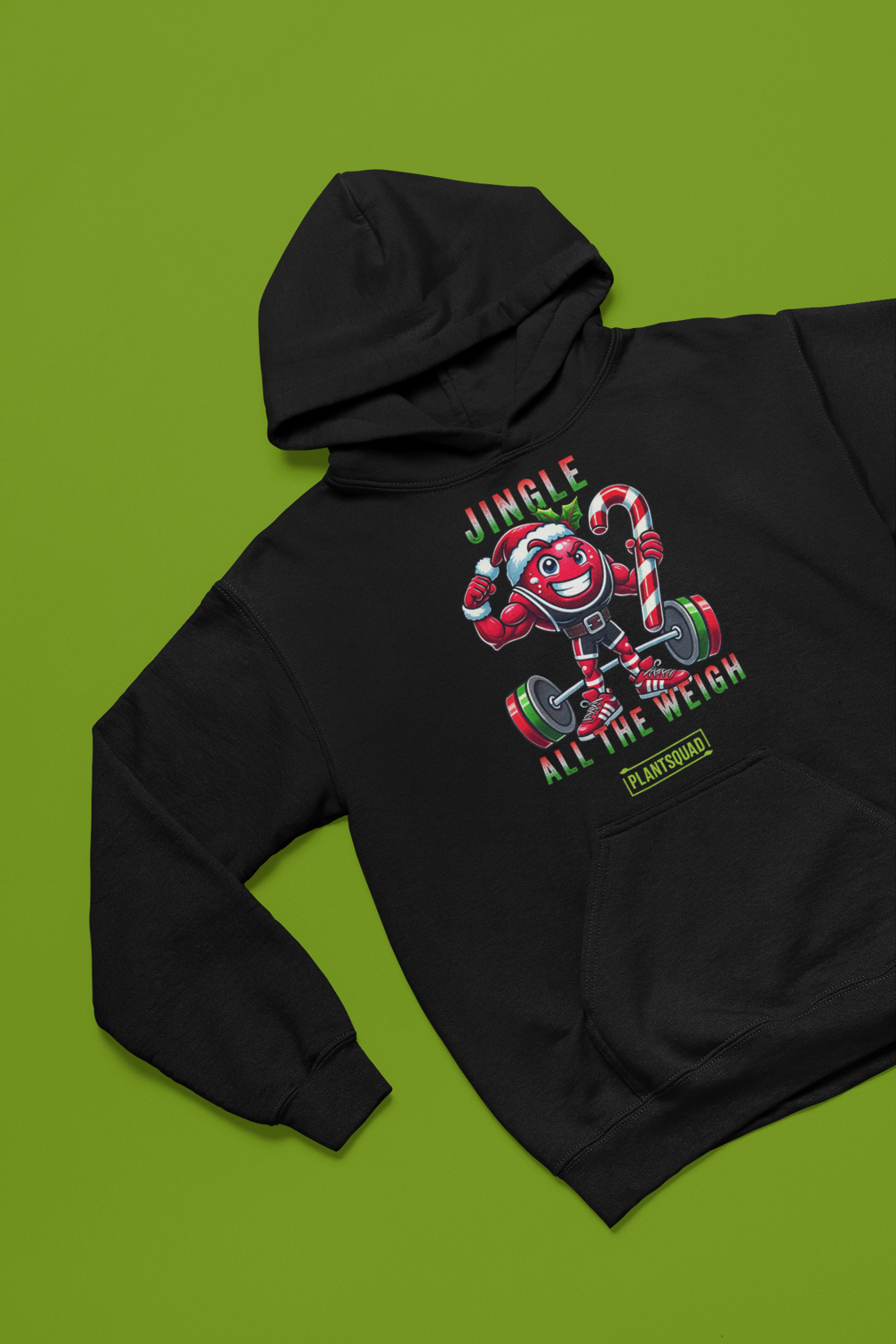 A picture of a hoodie featuring a strong looking cranberry cartoon character flexing its arms holding a candy cane. A small green logo "PLANTSQUAD" appears above the character, "JINGLE ALL THE WEIGH" below. Perfect for those embracing a plant-based or vegan lifestyle that are into fitness