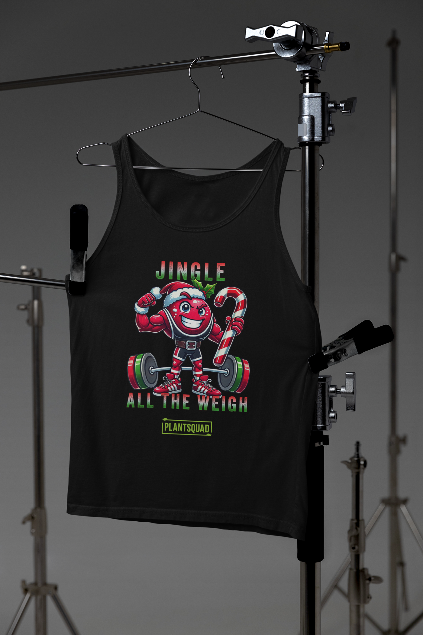 A picture of a tank top featuring a strong looking cranberry cartoon character flexing its arms holding a candy cane. A small green logo "PLANTSQUAD" appears above the character, "JINGLE ALL THE WEIGH" below. Perfect for those embracing a plant-based or vegan lifestyle that are into fitness
