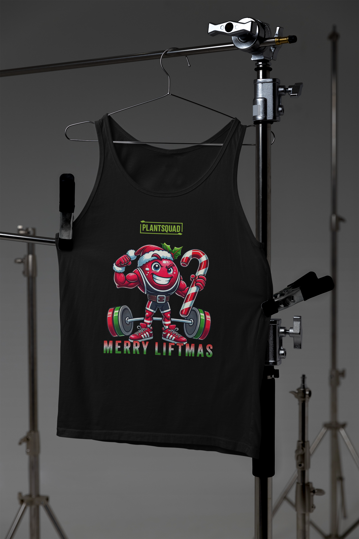 A picture of a tank top featuring a strong looking cranberry cartoon character flexing its arms holding a candy cane. A small green logo "PLANTSQUAD" appears above the character, "MERRY LIFTMAS" below. Perfect for those embracing a plant-based or vegan lifestyle that are into fitness