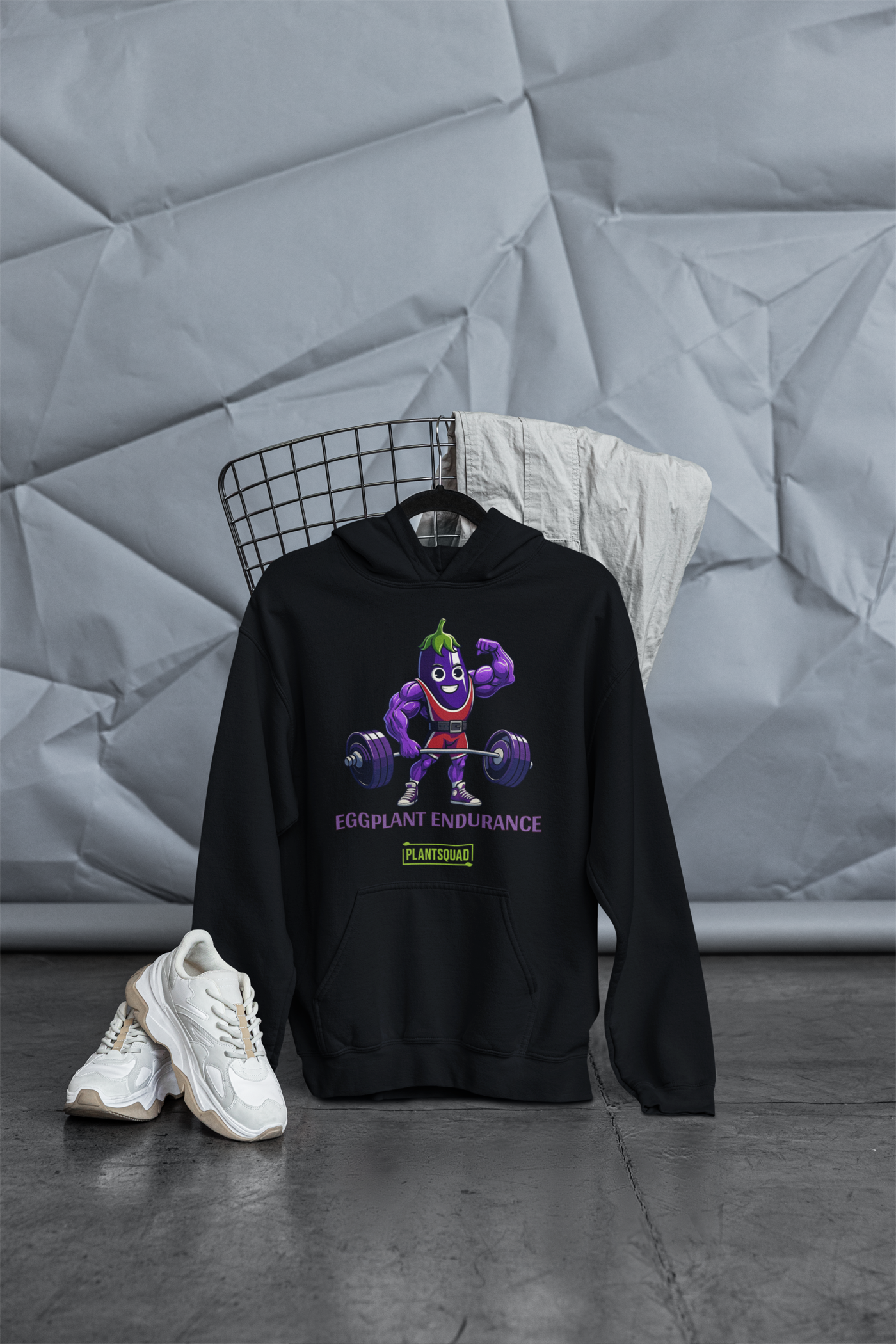 A Plantsquad Eggplant "Eggplant Endurance" - Unisex Hoodie featuring a cartoon eggplant with muscular arms, lifting a barbell with red weights. The text below reads "EGGPLANT ENDURANCE" in purple and "PLANTSQUAD" in green. This playful design, perfect for those embracing a vegan lifestyle, adds a fun and sporty touch to the hoodie.