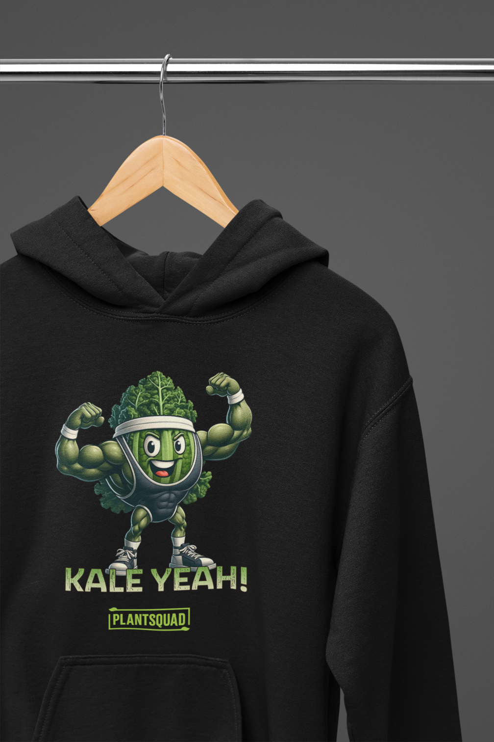 A Plantsquad Kale "Kale Yeah!" - Unisex Hoodie featuring a cartoon illustration of muscular kale wearing a headband and flexing its arms. Below the image, text reads "KALE YEAH!" and "PLANTSQUAD" in green and yellow, perfect for those embracing a vegan lifestyle.