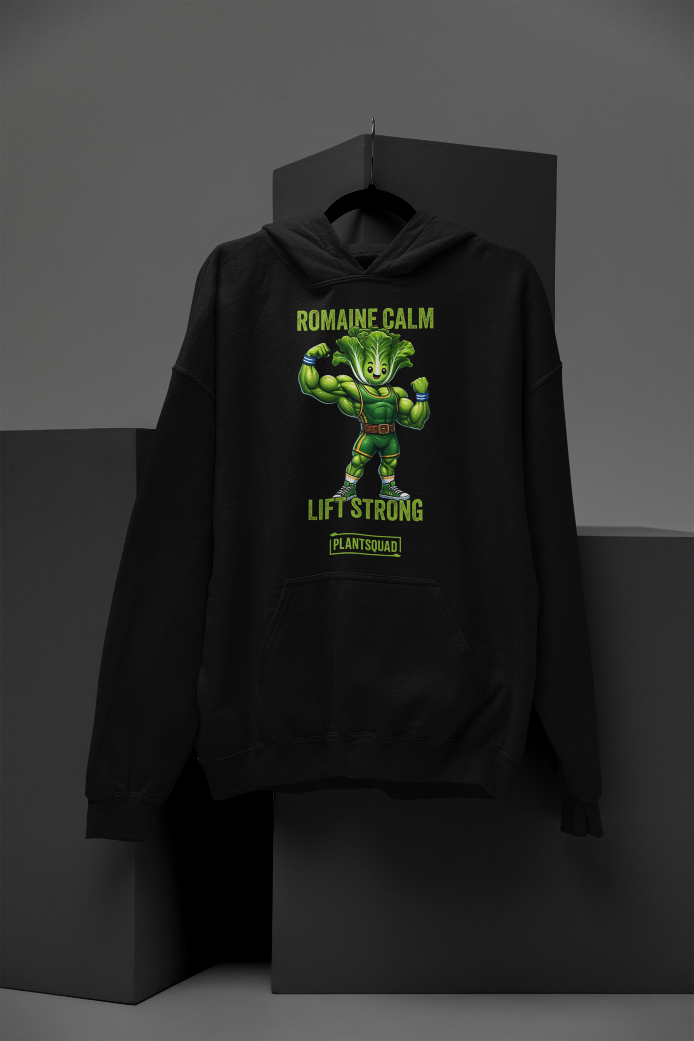 The Plantsquad Lettuce "Romaine Calm Lift Strong" - Unisex Hoodie features a muscular green vegetable character flexing its arms. The text above the character reads "ROMAINE CALM," and below it reads "LIFT STRONG." Embrace the vegan lifestyle with "PLANTSQUAD" displayed at the bottom. Perfect plant-based clothing for your workouts!