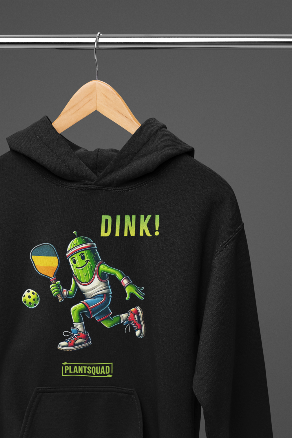A hoodie featuring a pickle playing pickleball. There is a caption listed as "Dink!", with a small green logo "PLANTSQUAD" underneath. Perfect for those who love pickleball.