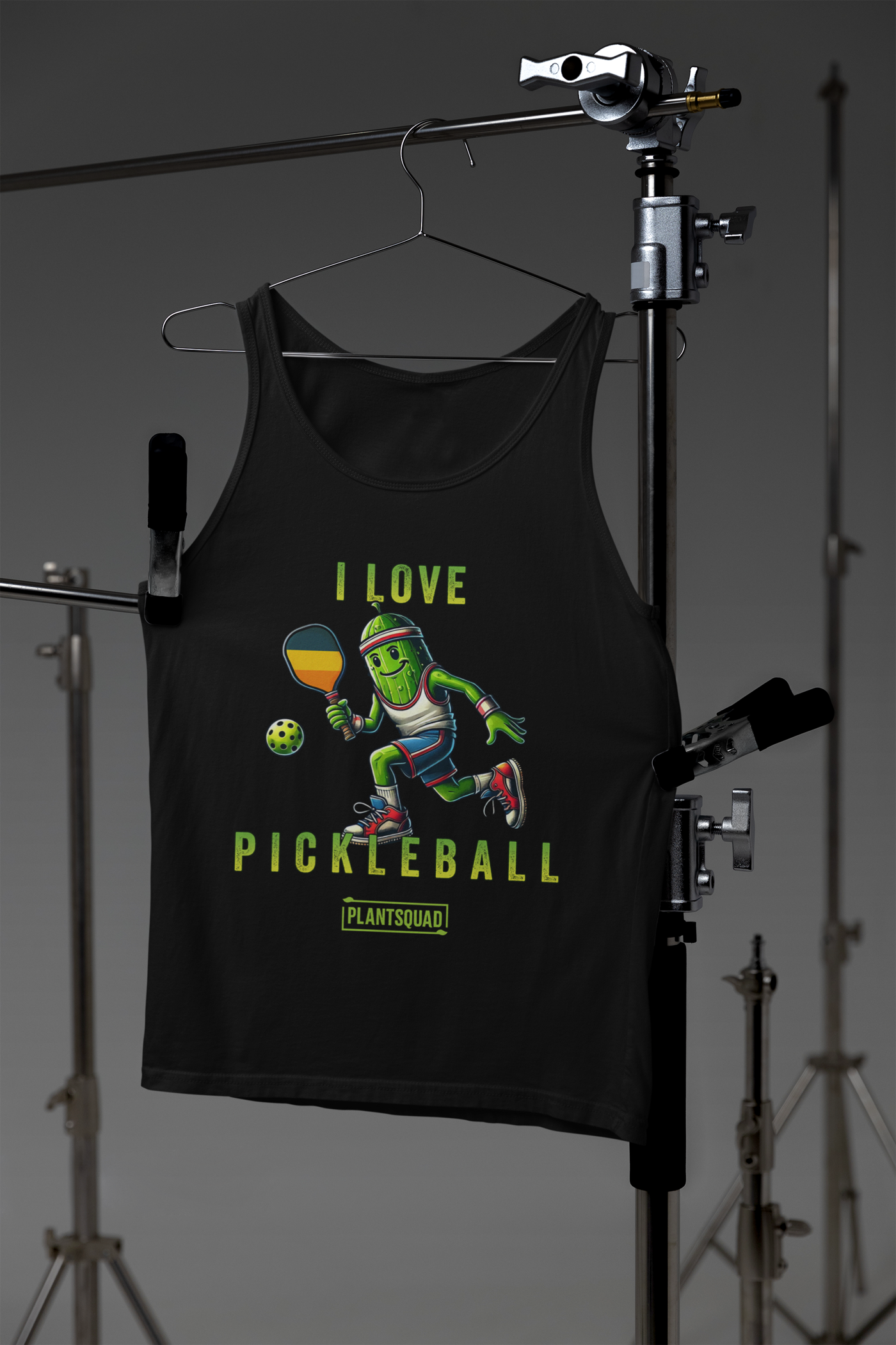 A hanging Tank Top featuring a pickle playing pickleball. There is a caption listed as "I Love Pickleball", with a small green logo "PLANTSQUAD" underneath. Perfect for those who love pickleball.