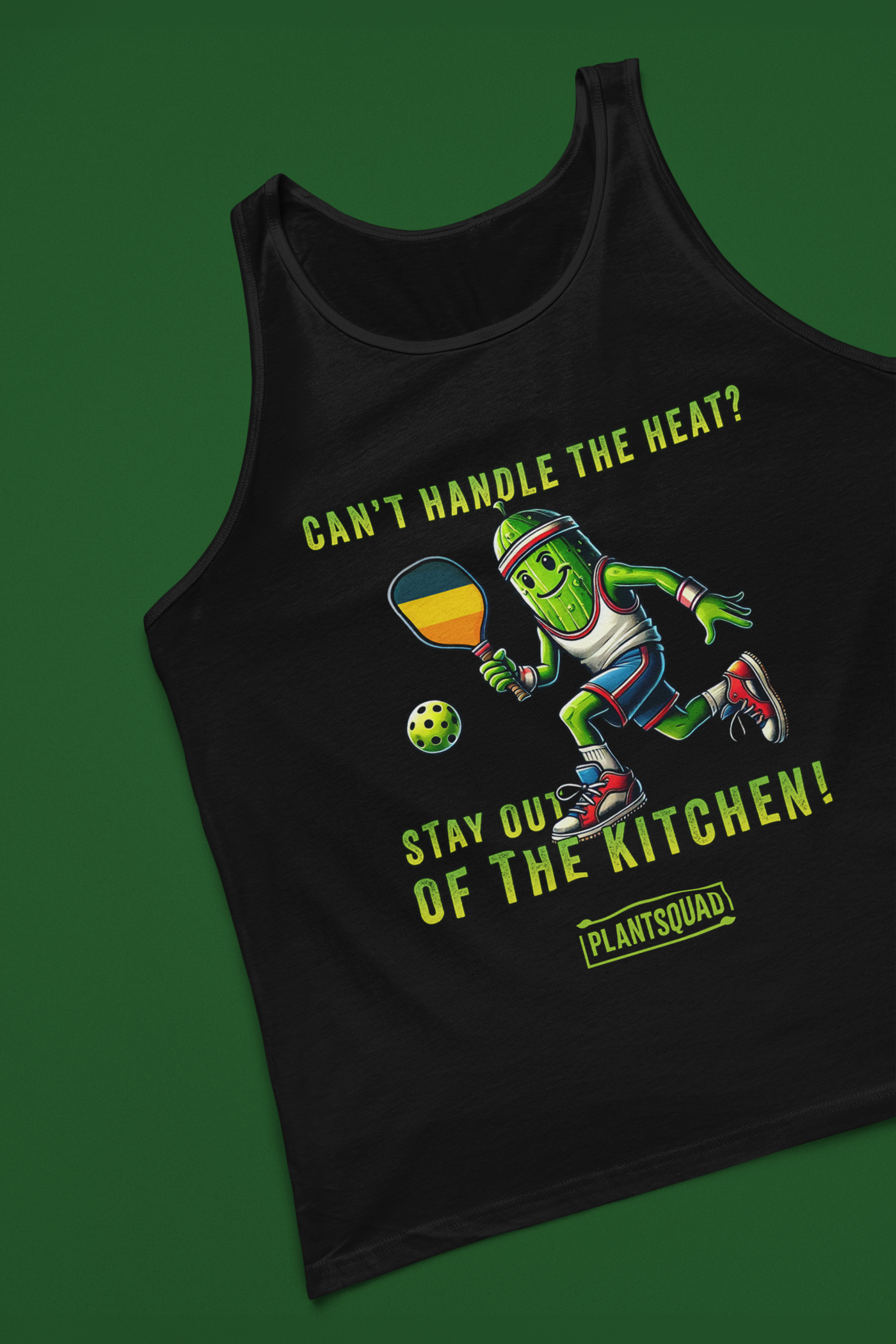 A tank top featuring a pickle playing pickleball. There is a caption listed as "Can't Handle The Heat? Stay Out Of The Kitchen!", with a small green logo "PLANTSQUAD" underneath. Perfect for those who love pickleball.