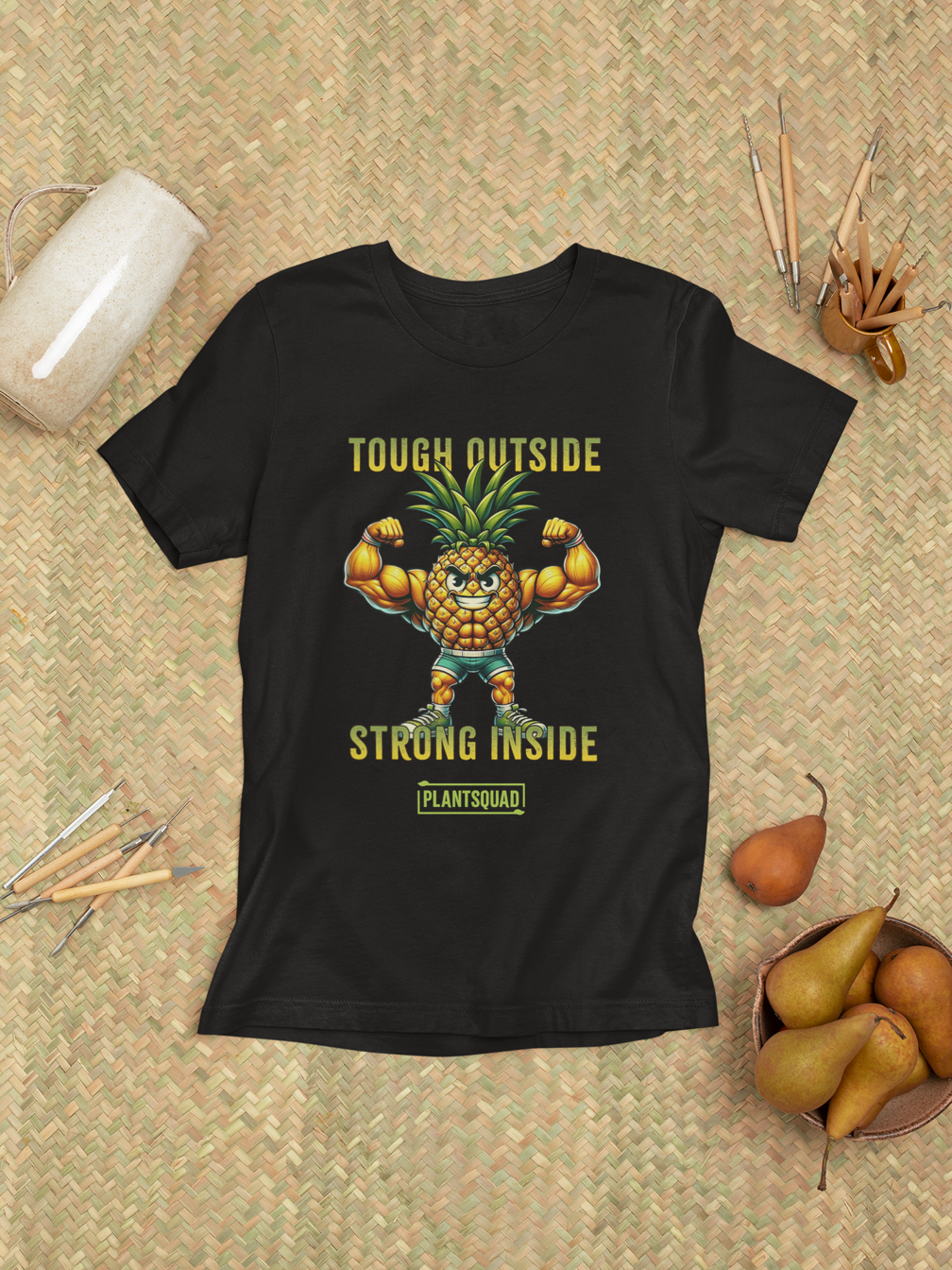 A black workout T-shirt features a muscular anthropomorphic pineapple flexing its biceps. Above the pineapple is the text "Tough Outside" and below it reads "Strong Inside." At the bottom, there's a green box with the word "Plantsquad Pineapple 'Tough Outside Strong Inside' - Unisex T-Shirt," perfect for anyone embracing a plant-based lifestyle.