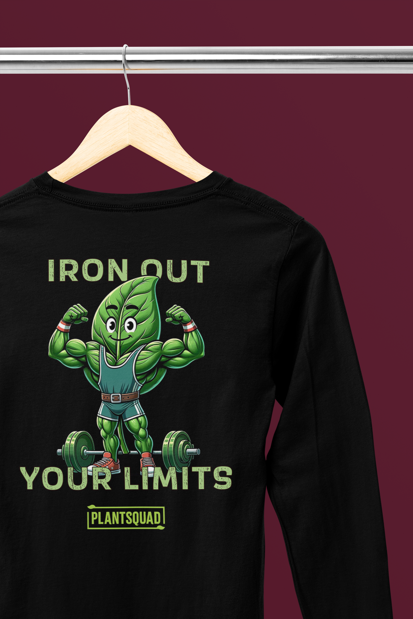 A Plantsquad Spinach "Iron Out Your Limits" - Unisex Long Sleeve T-Shirt features an illustration of a muscular green leaf character lifting a barbell and flexing its arms. Perfect for fitness enthusiasts embracing a vegan lifestyle, the text above and below the character reads, "IRON OUT YOUR LIMITS" and "PLANTSQUAD," respectively.