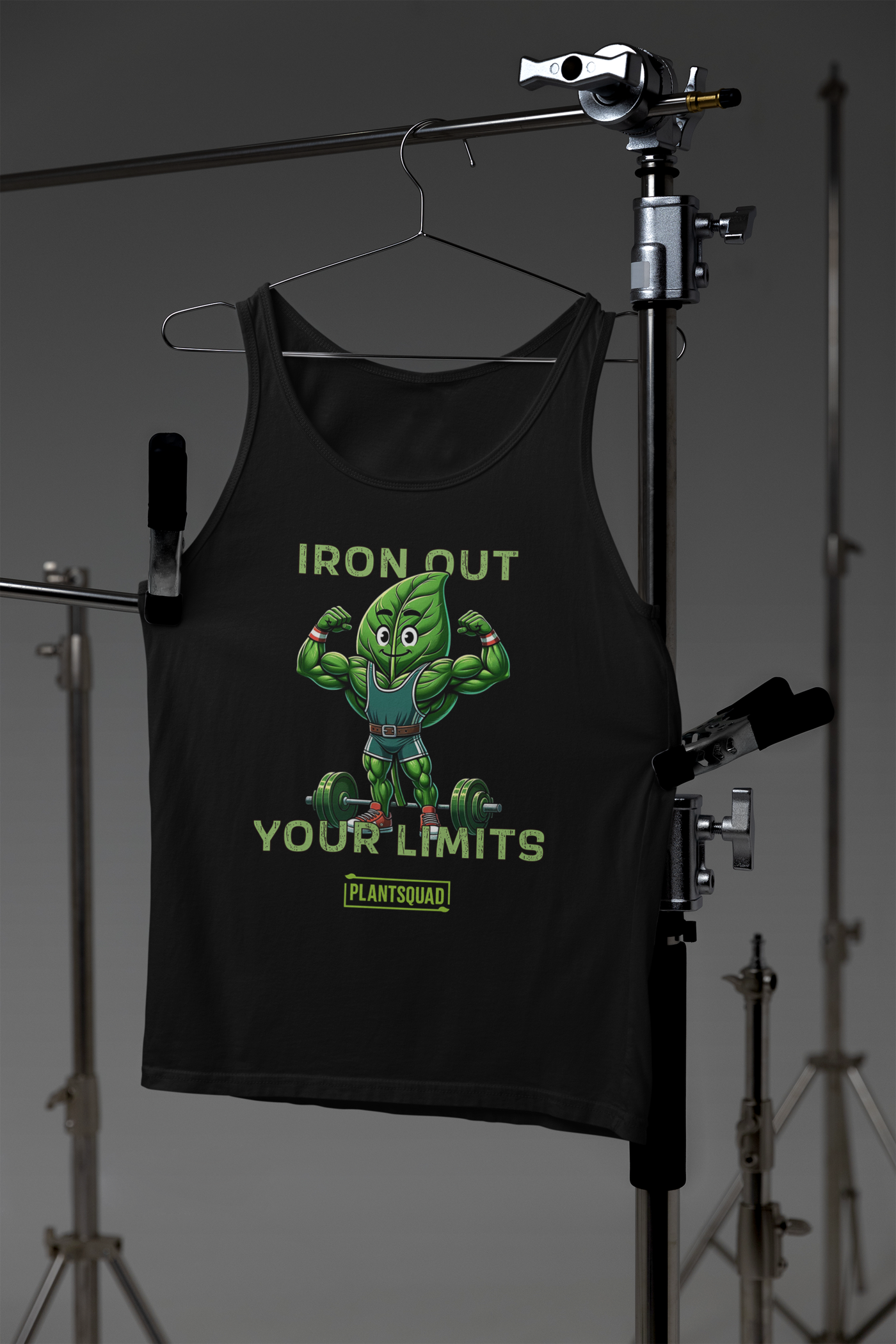 A Plantsquad Spinach "Iron Out Your Limits" - Unisex Tank Top features a cartoon muscular leaf character lifting weights, with the text "IRON OUT YOUR LIMITS" above and below the character, perfect for gym enthusiasts. Below the text is a logo with "PLANTSQUAD" written on it. Crafted from breathable fabric, it's ideal for a plant-based lifestyle.