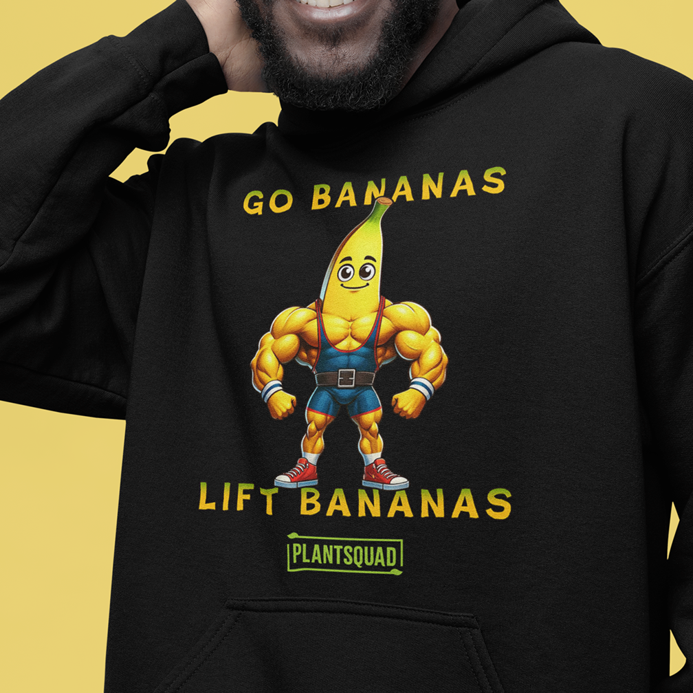 A person wearing a black hoodie with a cartoon banana character that has a muscular body. The text on the hoodie reads "GO BANANAS, LIFT BANANAS" with "PLANTSQUAD" underneath. The person is smiling against a yellow background.