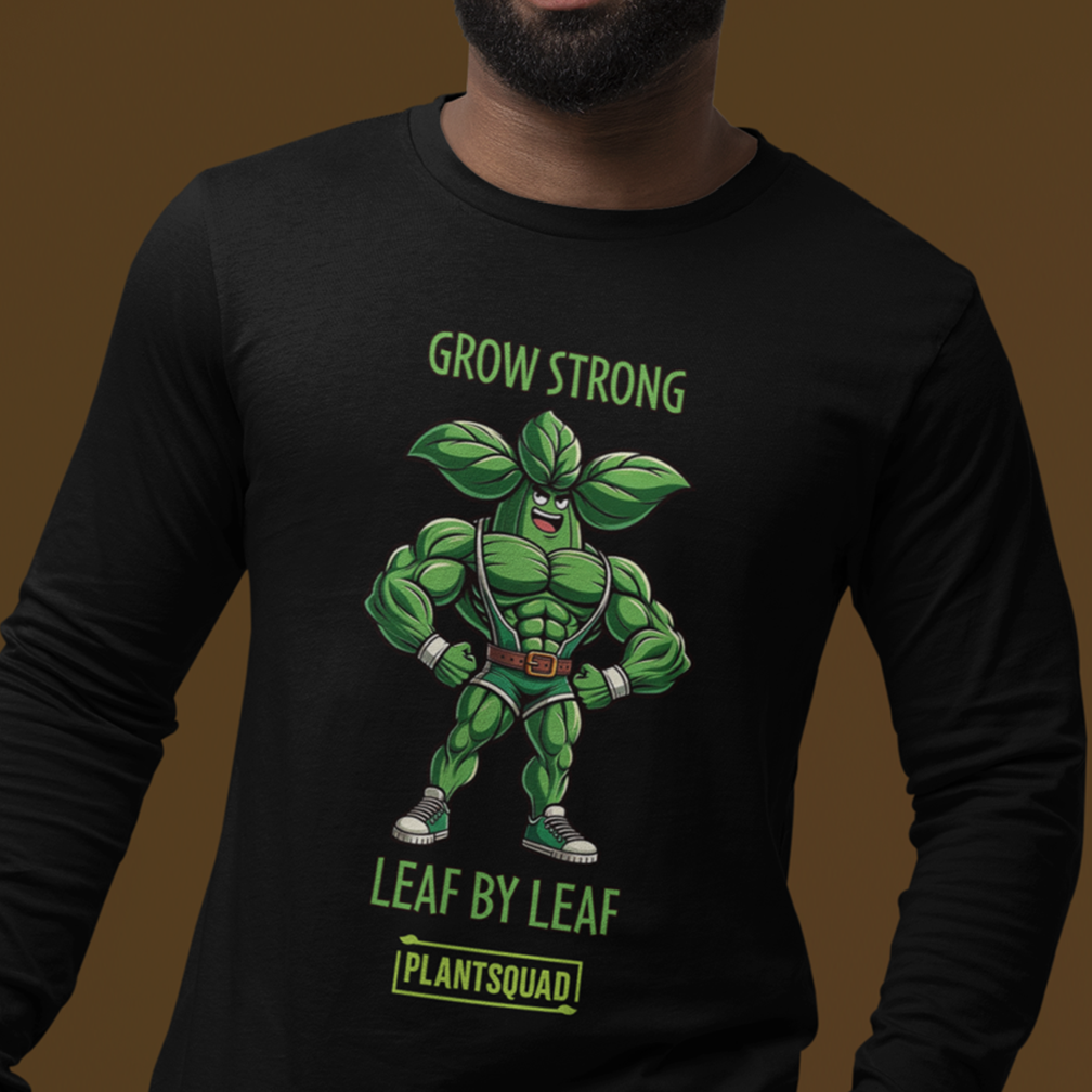 A person wearing a black long-sleeve shirt featuring an illustration of a muscular green plant character with a cape and sneakers. The text above the character reads "GROW STRONG", and below it reads "LEAF BY LEAF", with "PLANTSQUAD" at the bottom.