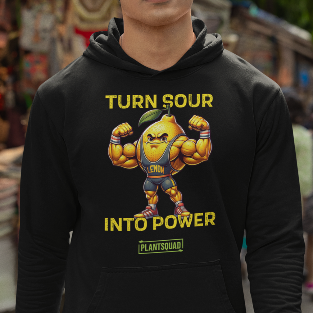 A person wearing a black hoodie featuring a muscular cartoon lemon character flexing its arms. The text on the hoodie reads "Turn Sour Into Power" with "Plantsquad" written below. The background shows a blurred outdoor setting.