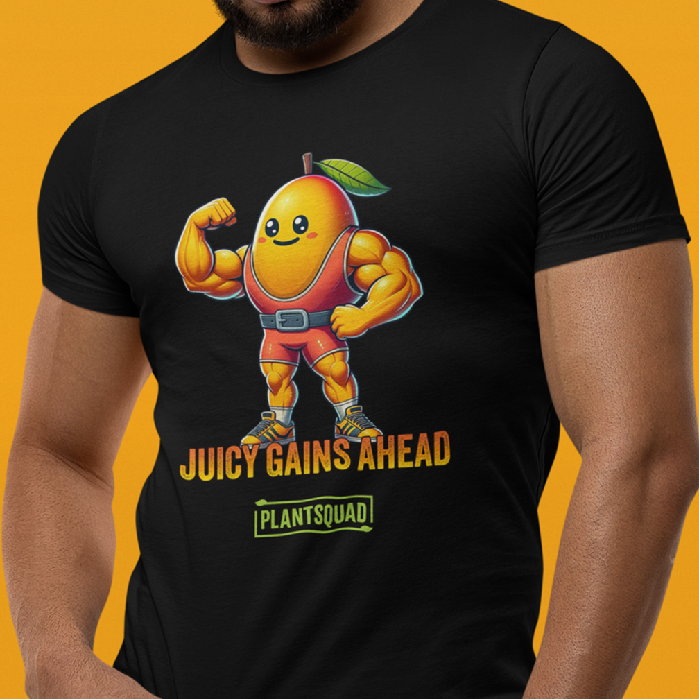 A person wears a black T-shirt featuring a cartoon mango character with muscular arms, flexing in a bodybuilder pose. The text below reads "JUICY GAINS AHEAD" followed by "PLANTSQUAD" in a green box. The background is a vibrant orange color.