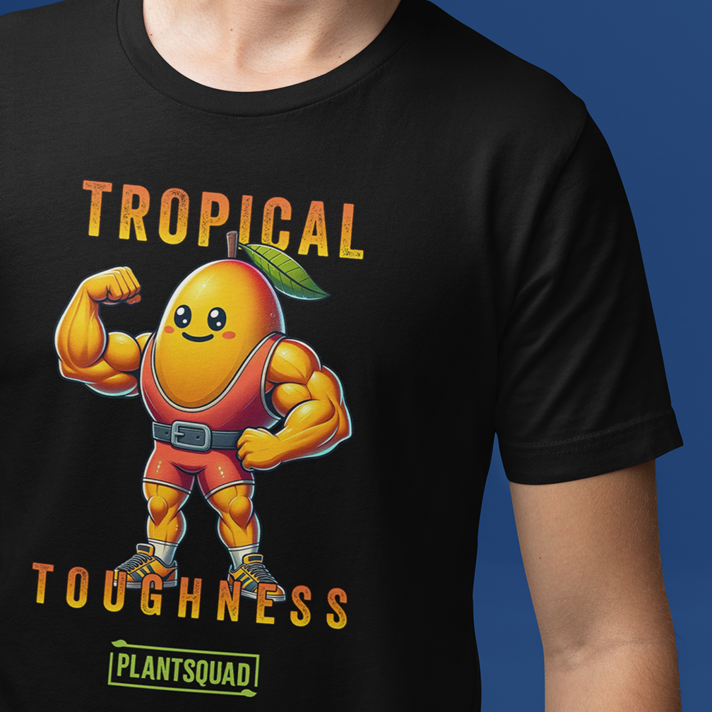 A person is wearing a black T-shirt with an illustration of a muscular, anthropomorphic mango in a superhero outfit flexing its biceps. The text above the mango reads "Tropical Toughness," and below it is the word "Plantsquad.