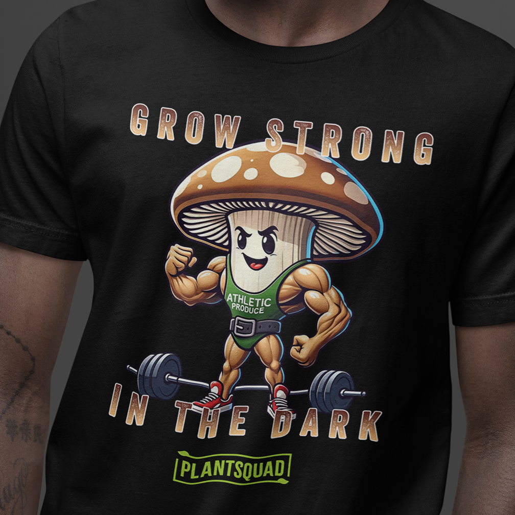 A person wearing a black T-shirt features a muscular anthropomorphic mushroom lifting barbells. The text above the character reads "GROW STRONG IN THE DARK," and text below reads "PLANTSQUAD." The mushroom wears a tank top labeled "ATHLETIC PRODUCE.