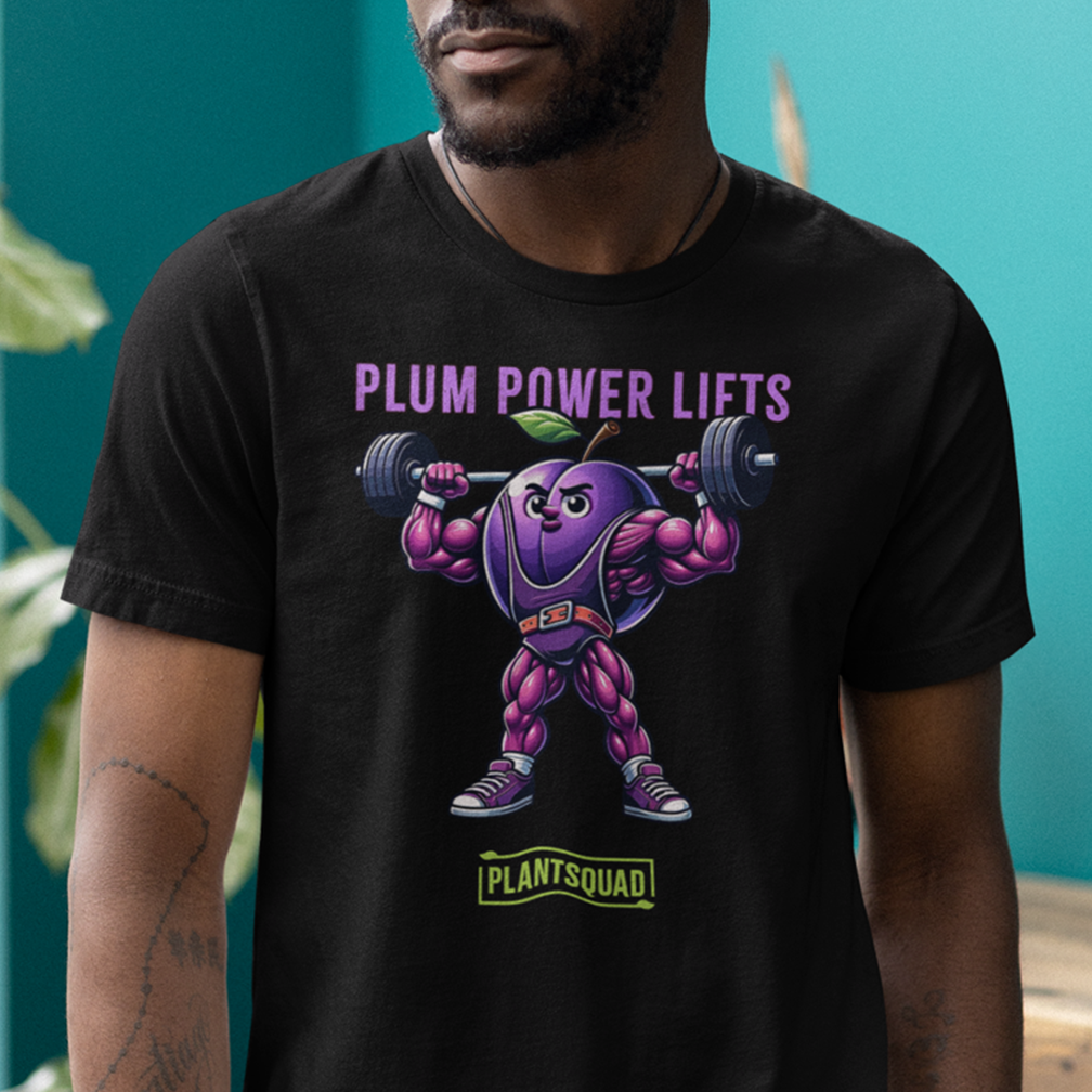 A person is wearing a black t-shirt featuring a muscular, anthropomorphic plum lifting a barbell. The text above the plum reads "PLUM POWER LIFTS," and the text below reads "PLANTSQUAD." The background is a turquoise wall with some green leaves visible.