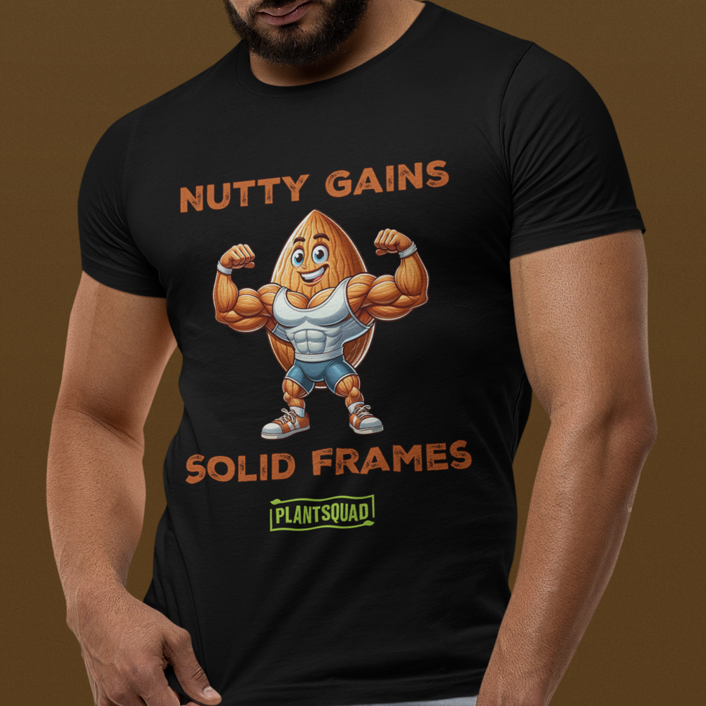 A black t-shirt displaying a muscular almond character flexing its biceps. Above the character, text reads "NUTTY GAINS," and below, it says "SOLID FRAMES." A green and yellow logo at the bottom reads "PLANTSQUAD.