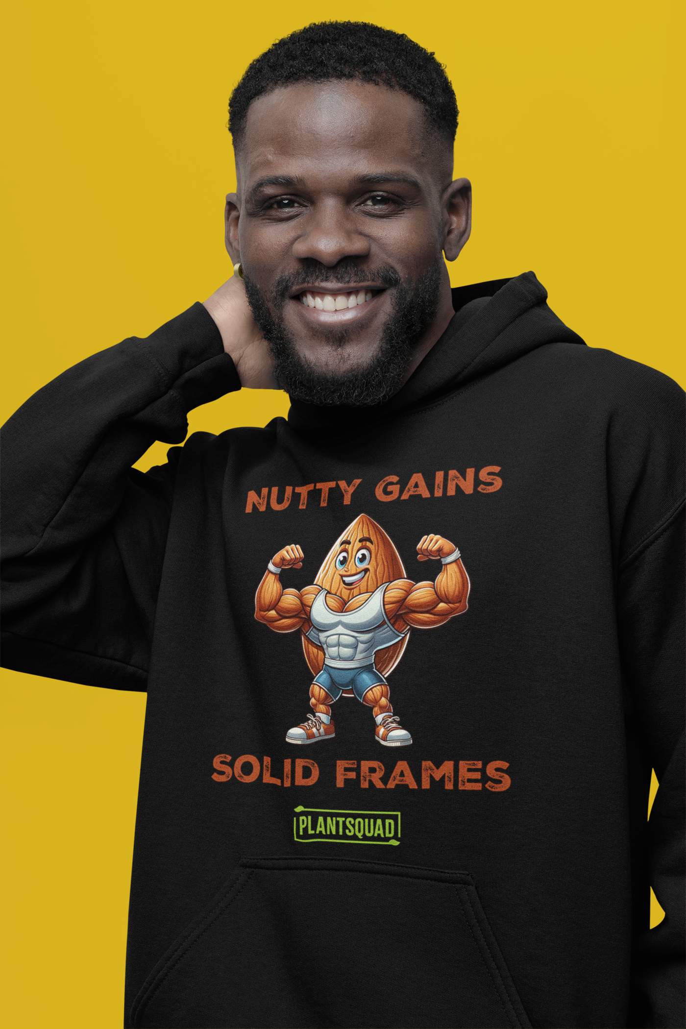 A black Plantsquad Almond "Nutty Gains Solid Frames" - Unisex Hoodie displays a muscular peanut character flexing its biceps with the text "Nutty Gains" above and "Solid Frames" below. The logo "Plant Squad" is at the bottom, perfect for gym enthusiasts. The design is bold, humorous, and fitness-themed.