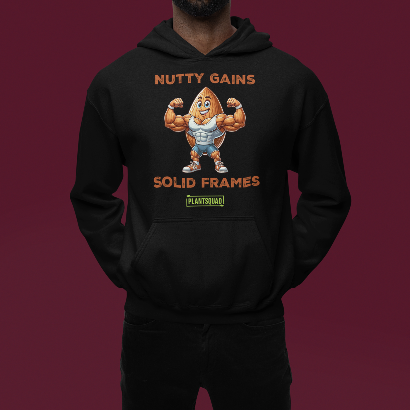 A black Plantsquad Almond "Nutty Gains Solid Frames" - Unisex Hoodie displays a muscular peanut character flexing its biceps with the text "Nutty Gains" above and "Solid Frames" below. The logo "Plant Squad" is at the bottom, perfect for gym enthusiasts. The design is bold, humorous, and fitness-themed.