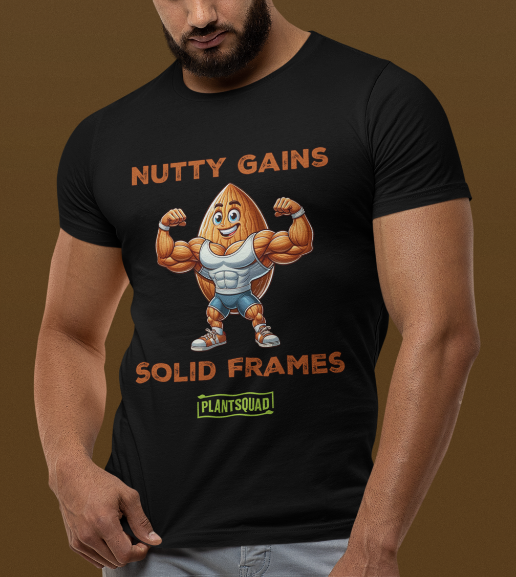 A black T-shirt features a muscular cartoon peanut character flexing its arms. Above the character, text reads "Nutty Gains," and below, "Solid Frames." The Plantsquad Almond "Nutty Gains Solid Frames" - Unisex T-Shirt logo appears at the bottom in green.