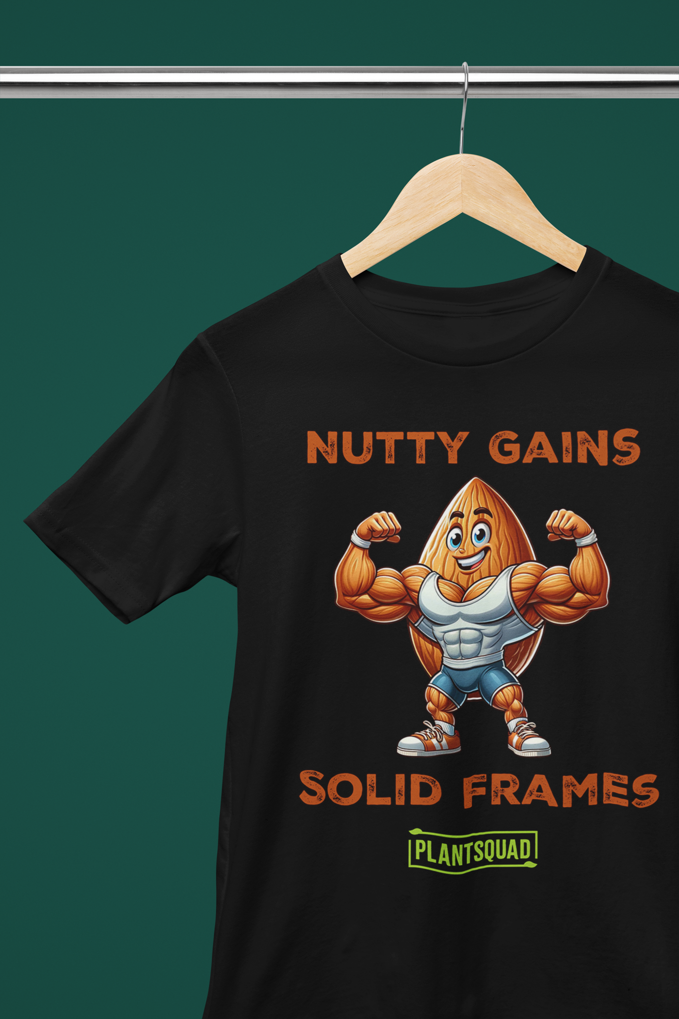 A black T-shirt features a muscular cartoon peanut character flexing its arms. Above the character, text reads "Nutty Gains," and below, "Solid Frames." The Plantsquad Almond "Nutty Gains Solid Frames" - Unisex T-Shirt logo appears at the bottom in green.