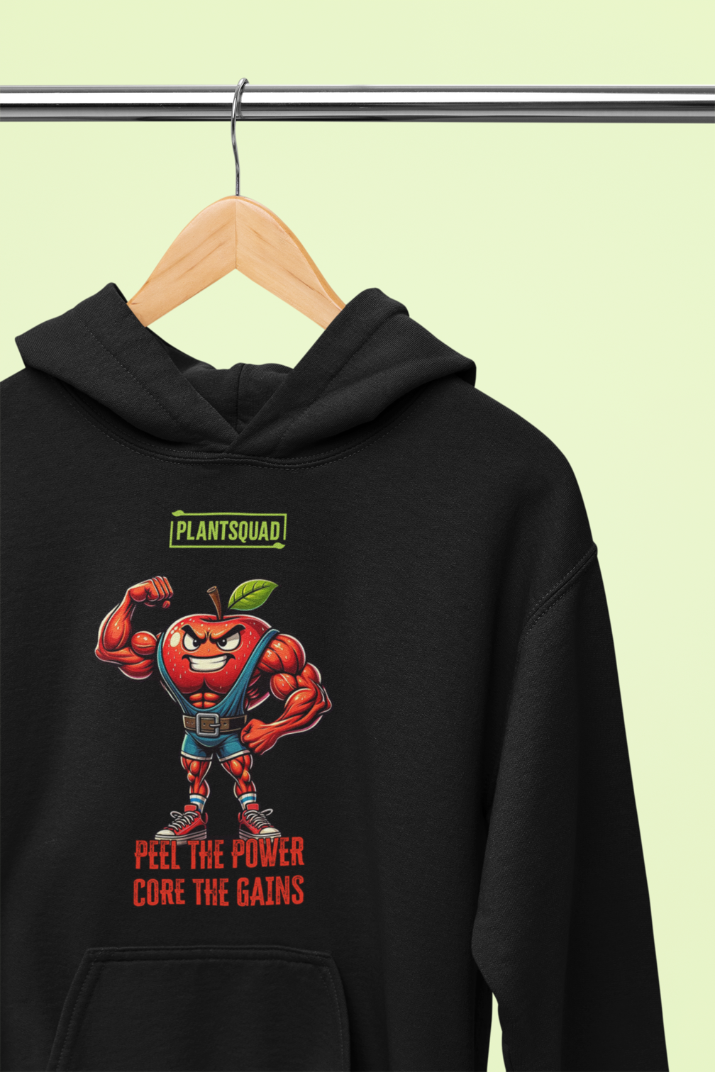 The Plantsquad Apple "Peel The Power Core The Gains" - Unisex Hoodie features a black vegan design with a muscular, anthropomorphic apple character in a fitness pose. The red apple, with a determined expression, is wearing a weightlifting belt. Above, it says 'PLANTSQUAD,' and below, 'PEEL THE POWER, CORE THE GAINS' in bold red text. Perfect for embracing your plant-based lifestyle.