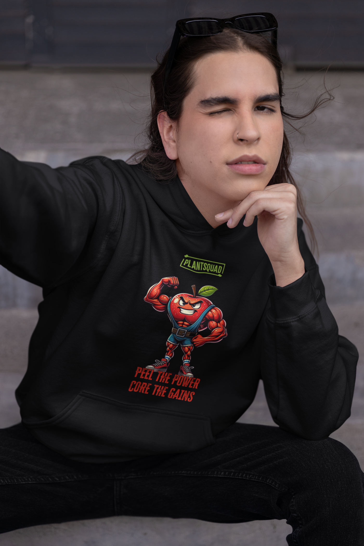 The Plantsquad Apple "Peel The Power Core The Gains" - Unisex Hoodie features a black vegan design with a muscular, anthropomorphic apple character in a fitness pose. The red apple, with a determined expression, is wearing a weightlifting belt. Above, it says 'PLANTSQUAD,' and below, 'PEEL THE POWER, CORE THE GAINS' in bold red text. Perfect for embracing your plant-based lifestyle.