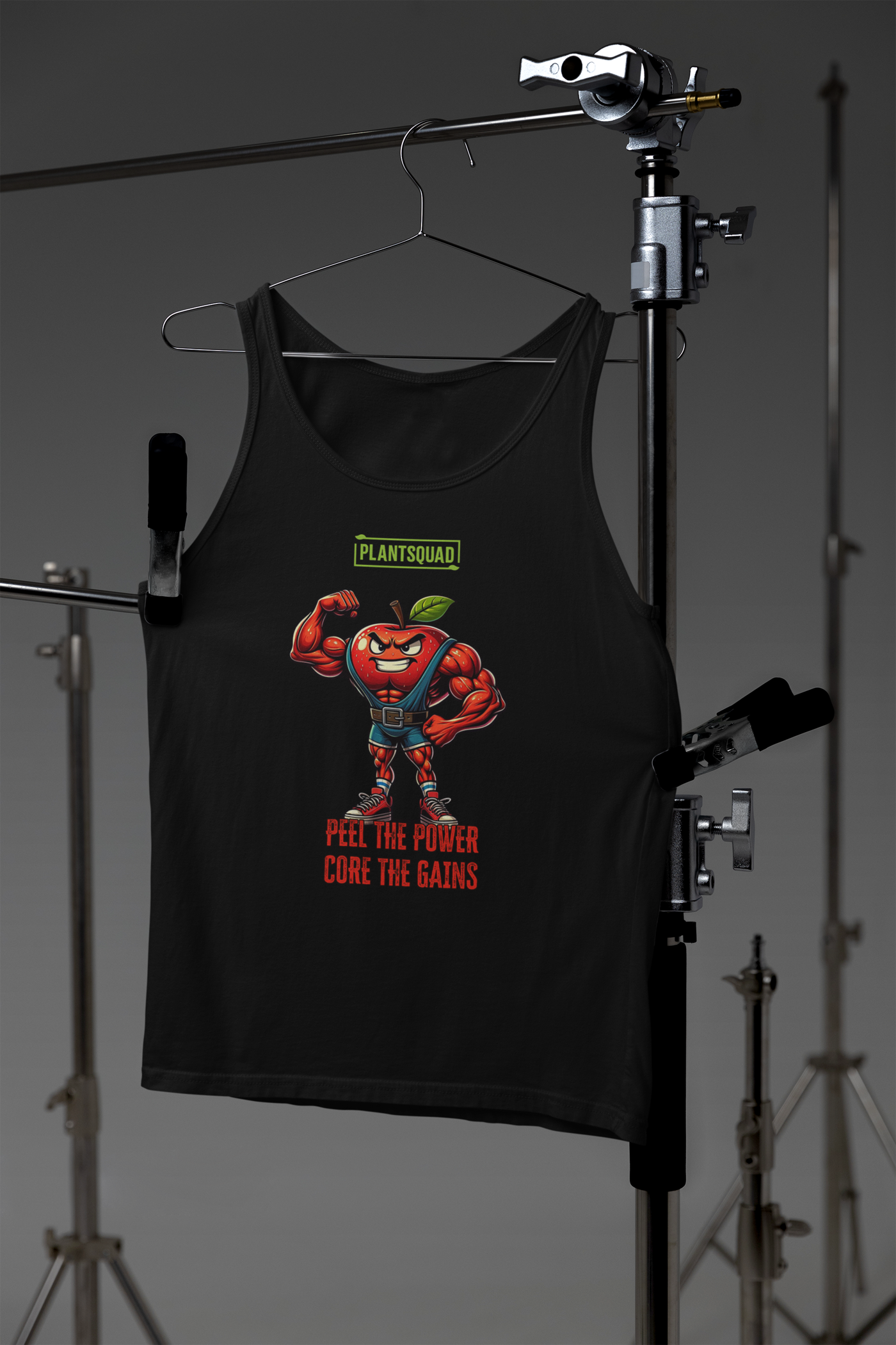 The Plantsquad Apple "Peel The Power Core The Gains" - Unisex Tank Top features a muscular anthropomorphic red apple character flexing its arm. Above it, the text reads "PLANTSQUAD," and below, "PEEL THE POWER, CORE THE GAINS" in bold letters. The apple character wears a weightlifting belt and sneakers, making it perfect for gym enthusiasts who prefer breathable fabric and a vegan lifestyle.