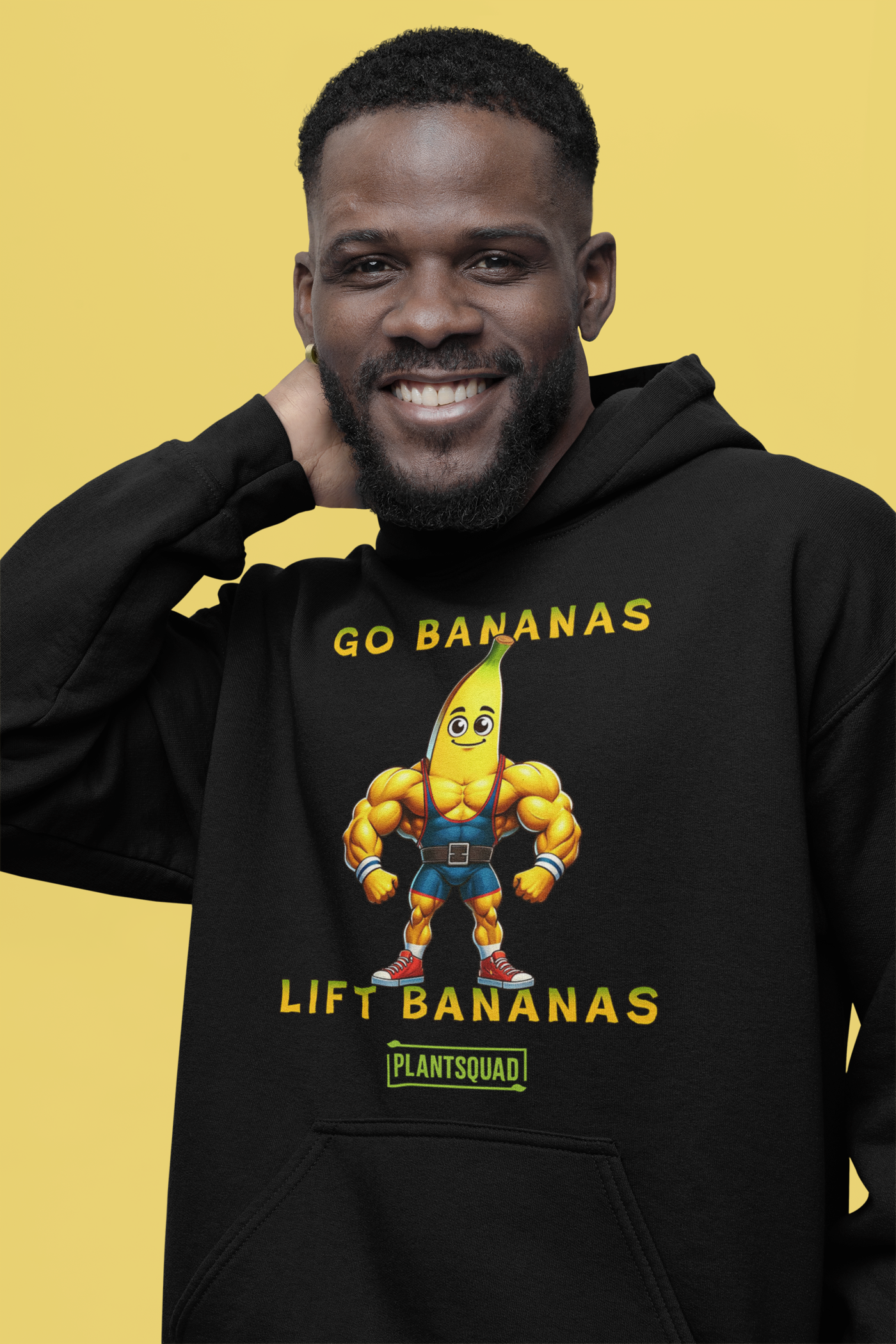 A black vegan hoodie featuring a muscular cartoon banana character flexing its arms. The text above the character reads "GO BANANAS" and below the character reads "LIFT BANANAS." There is a small "PLANTSQUAD" logo beneath the character, ideal for those embracing a plant-based lifestyle and weight lifting apparel. The product name is Plantsquad Banana "Go Bananas Lift Bananas" - Unisex Hoodie.