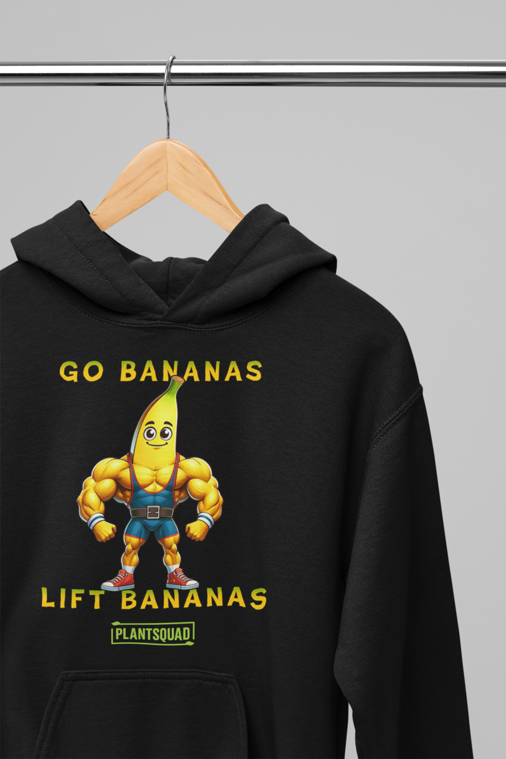 A black vegan hoodie featuring a muscular cartoon banana character flexing its arms. The text above the character reads "GO BANANAS" and below the character reads "LIFT BANANAS." There is a small "PLANTSQUAD" logo beneath the character, ideal for those embracing a plant-based lifestyle and weight lifting apparel. The product name is Plantsquad Banana "Go Bananas Lift Bananas" - Unisex Hoodie.