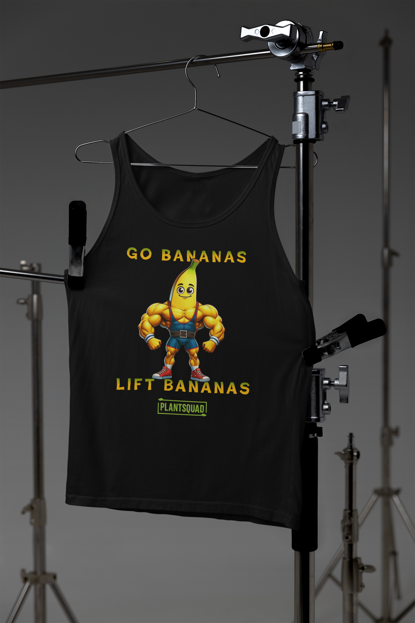 A Plantsquad Banana "Go Bananas Lift Bananas" - Unisex Tank Top featuring a cartoon banana character with a muscular body. The banana is wearing a weightlifting belt and black shorts. The text reads "GO BANANAS LIFT BANANAS" in yellow, with a small green box below containing the word "PLANTSQUAD." Perfect for gym enthusiasts embracing a plant-based lifestyle.