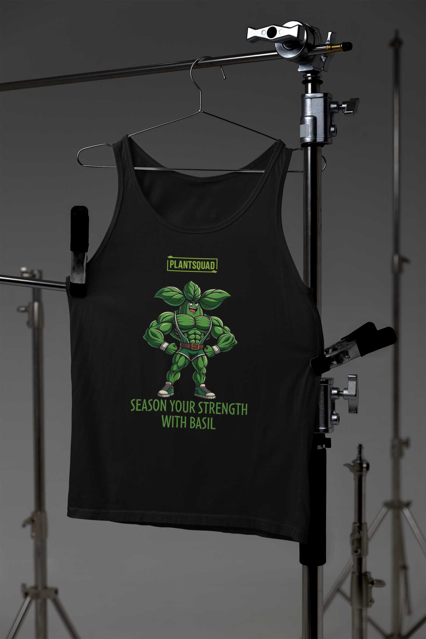 A black, plant-based tank top featuring a muscular, anthropomorphic basil plant character flexing its muscles. Above the character, text reads "PLANTSQUAD," and below it says "Season Your Strength with Basil." Perfect for those seeking vegan gym clothes or breathable workout apparel, this is the Plantsquad Basil "Season Your Strength With Basil" - Unisex Tank Top.