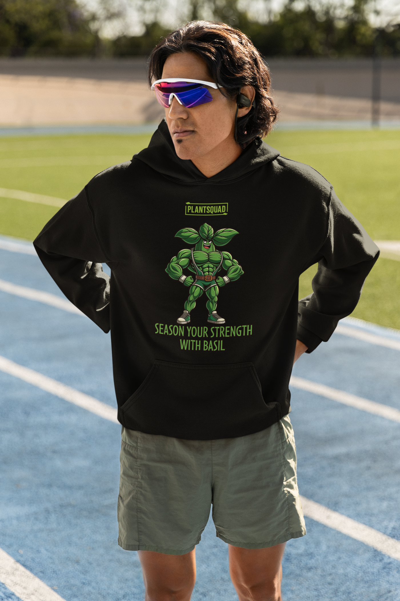 The Plantsquad Basil "Season Your Strength With Basil" - Unisex Hoodie features a muscular cartoon basil character, aptly named Basil, standing with arms crossed. Above Basil, a green logo reads "PLANTSQUAD." Below him, the text says, "SEASON YOUR STRENGTH WITH BASIL." Embrace the vegan lifestyle and cozy fabric while flaunting your love for weight lifting.