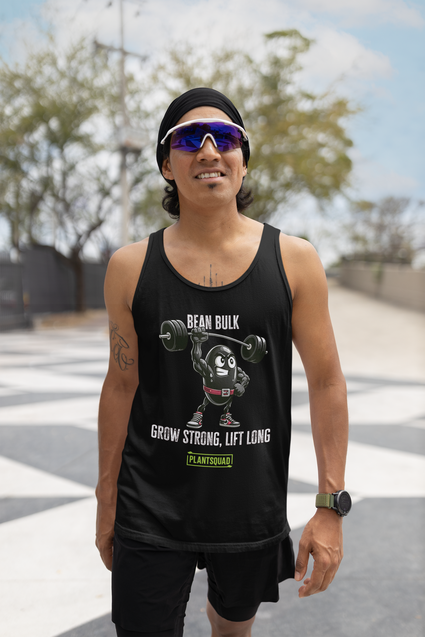 The Plantsquad Black Bean "Bean Bulk Grow Strong Lift Long" - Unisex Tank Top features a cartoon bean character lifting a barbell with the text "BEAN BULK" above and "GROW STRONG, LIFT LONG" below. Perfect for gym enthusiasts embracing a plant-based lifestyle, it has the logo "PLANTSQUAD" in green at the bottom. The bean wears red gloves, a red belt, and red shoes.