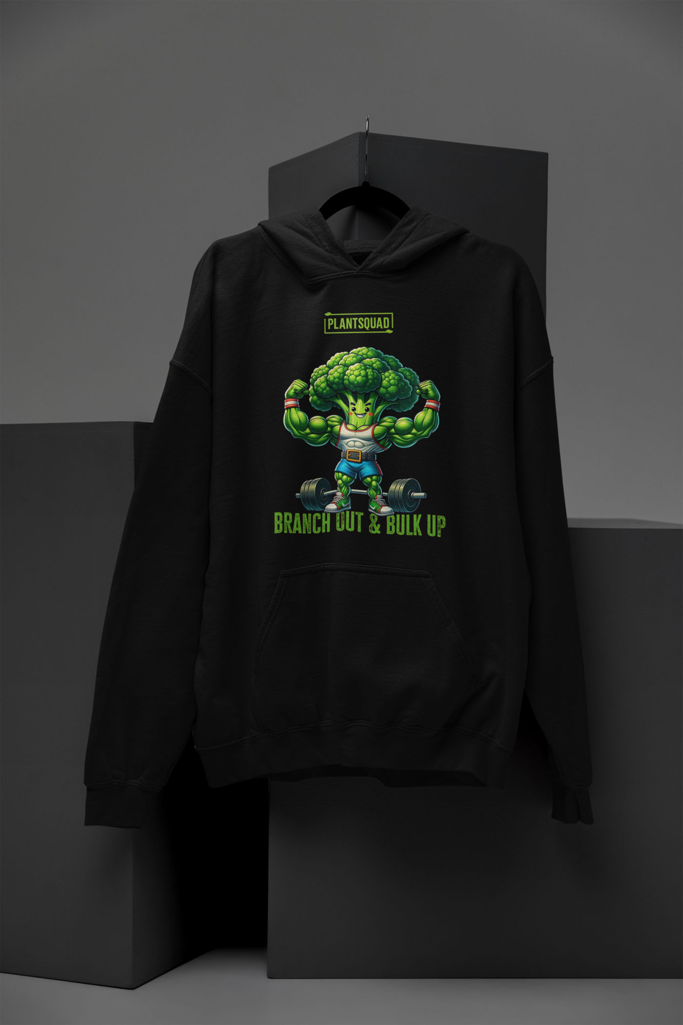 A Plantsquad Broccoli "Branch Out & Bulk Up" - Unisex Hoodie made from cozy fabric features an illustration of a muscular, anthropomorphic broccoli lifting dumbbells. The text above reads "PLANTSQUAD" and below reads "BRANCH OUT & BULK UP!" Perfect for those embracing a vegan lifestyle, the hoodie has a front pocket and a drawstring hood.