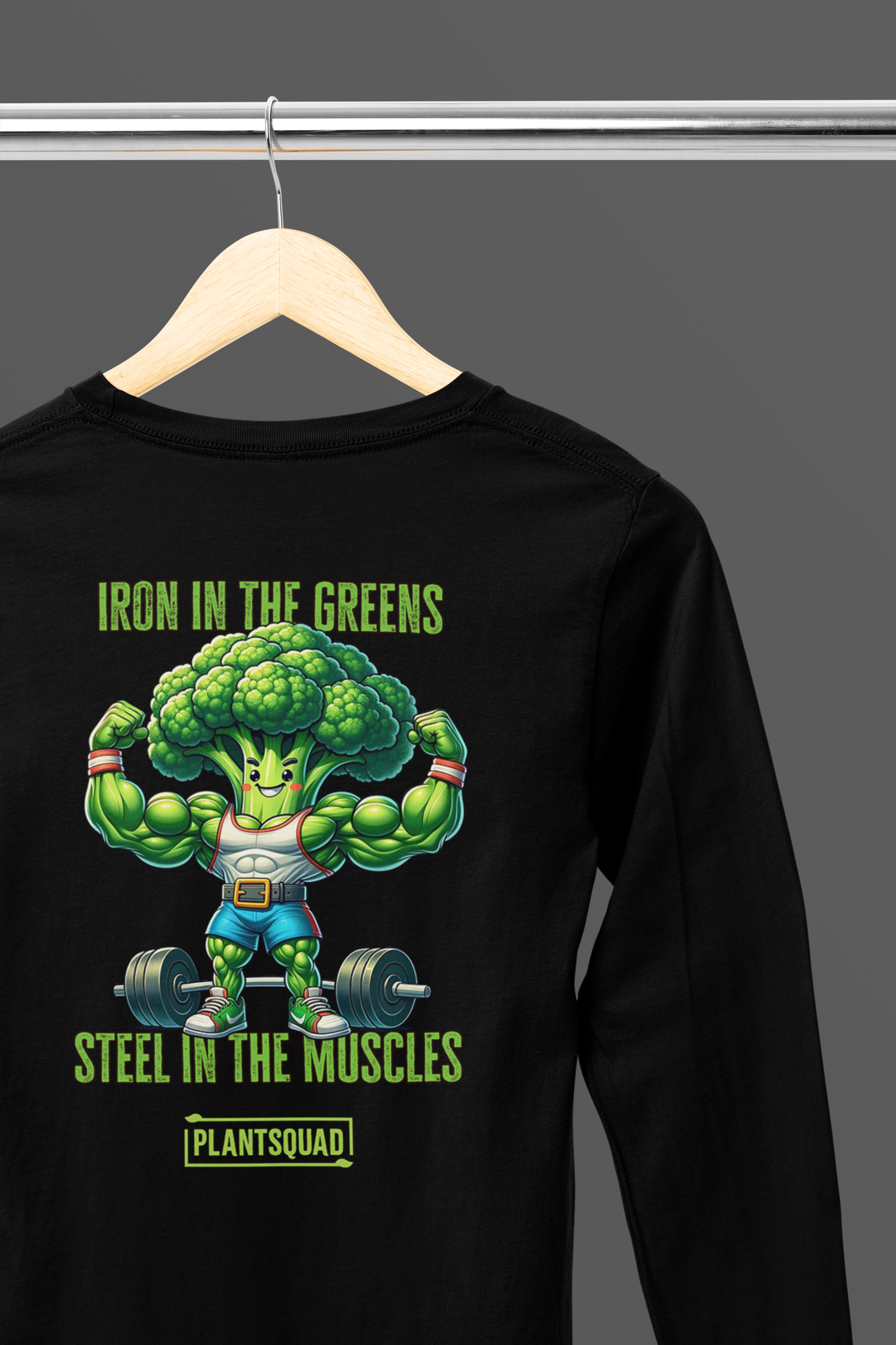 A Plantsquad Broccoli "Iron In The Greens Steel In The Muscles" - Unisex Long Sleeve T-Shirt featuring a muscly broccoli cartoon character lifting dumbbells. The text above reads, "Iron in the greens," and below, "Steel in the muscles." Perfect for fitness enthusiasts embracing a vegan lifestyle, the word "Plantsquad" is written at the bottom.