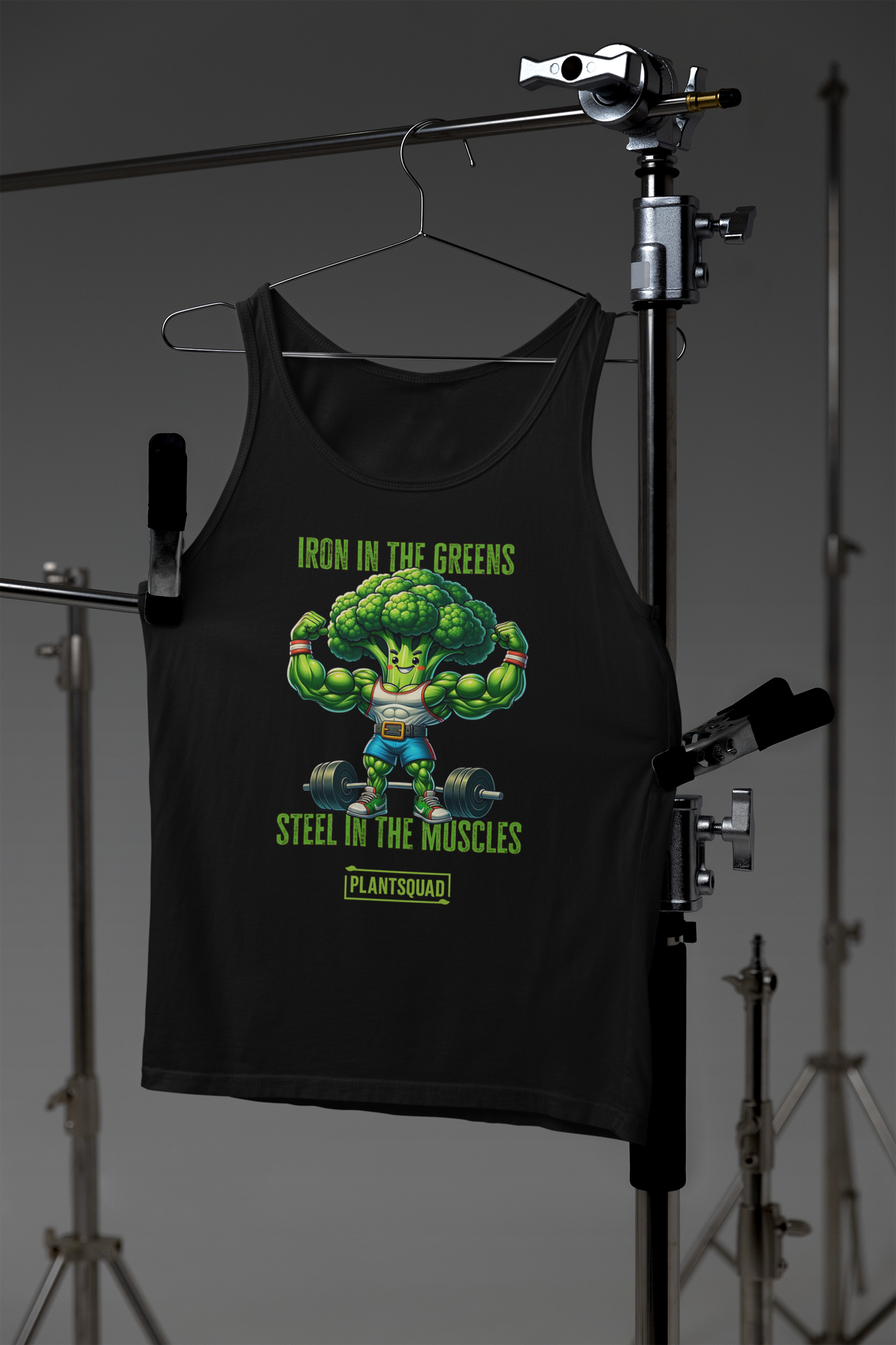 The Plantsquad Broccoli "Iron In The Greens Steel In The Muscles" - Unisex Tank Top features an illustration of a muscular broccoli character lifting weights. The text above reads "Iron in the Greens" and below reads "Steel in the Muscles" with "Plantsquad" at the bottom—perfect for gym enthusiasts embracing a plant-based lifestyle.