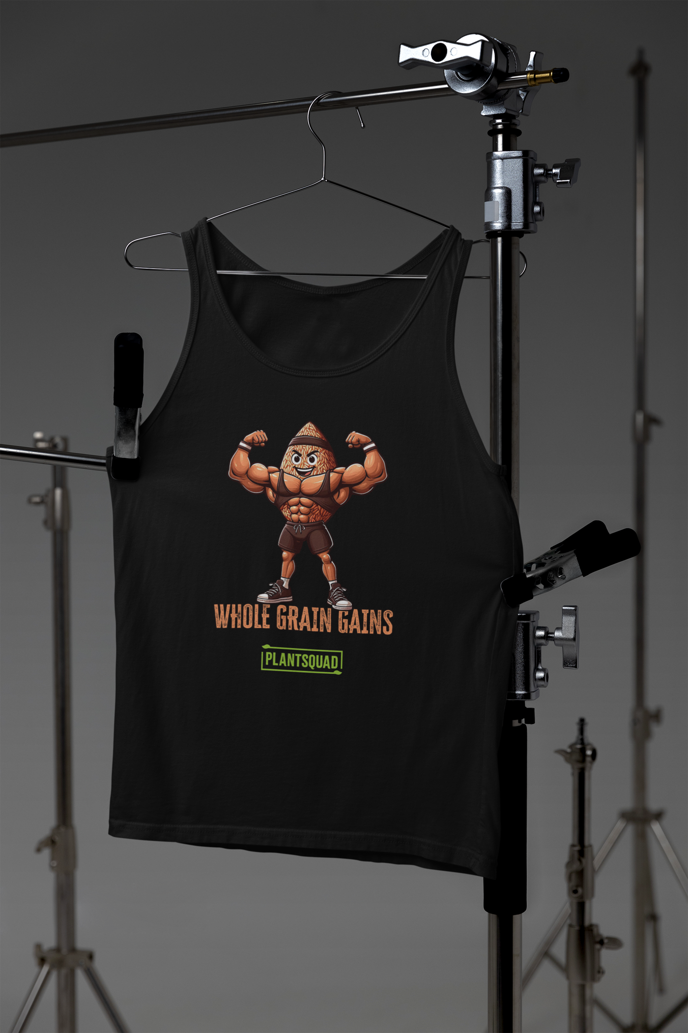 A black tank top features an illustration of a muscular, anthropomorphic grain of wheat flexing its biceps. Below the image, text reads "WHOLE GRAIN GAINS" in orange with the logo "PLANTSQUAD" in green underneath. Perfect for a plant-based lifestyle or as part of your vegan gym clothing collection, this is the Plantsquad Brown Rice "Whole Grain Gains" - Unisex Tank Top.