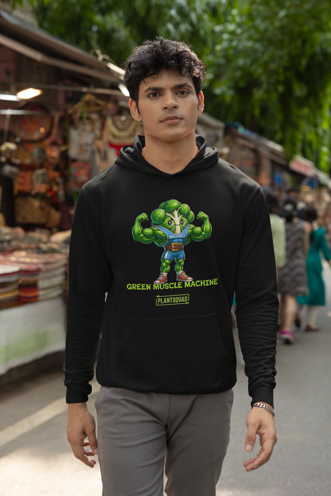 A black **Plantsquad Brussel Sprout "Green Muscle Machine" - Unisex Hoodie** featuring a muscular, anthropomorphic broccoli character flexing its arms. Text below the character reads "GREEN MUSCLE MACHINE" with "PLANTSQUAD" underneath—perfect for those embracing a plant-based lifestyle and seeking stylish vegan gym wear.