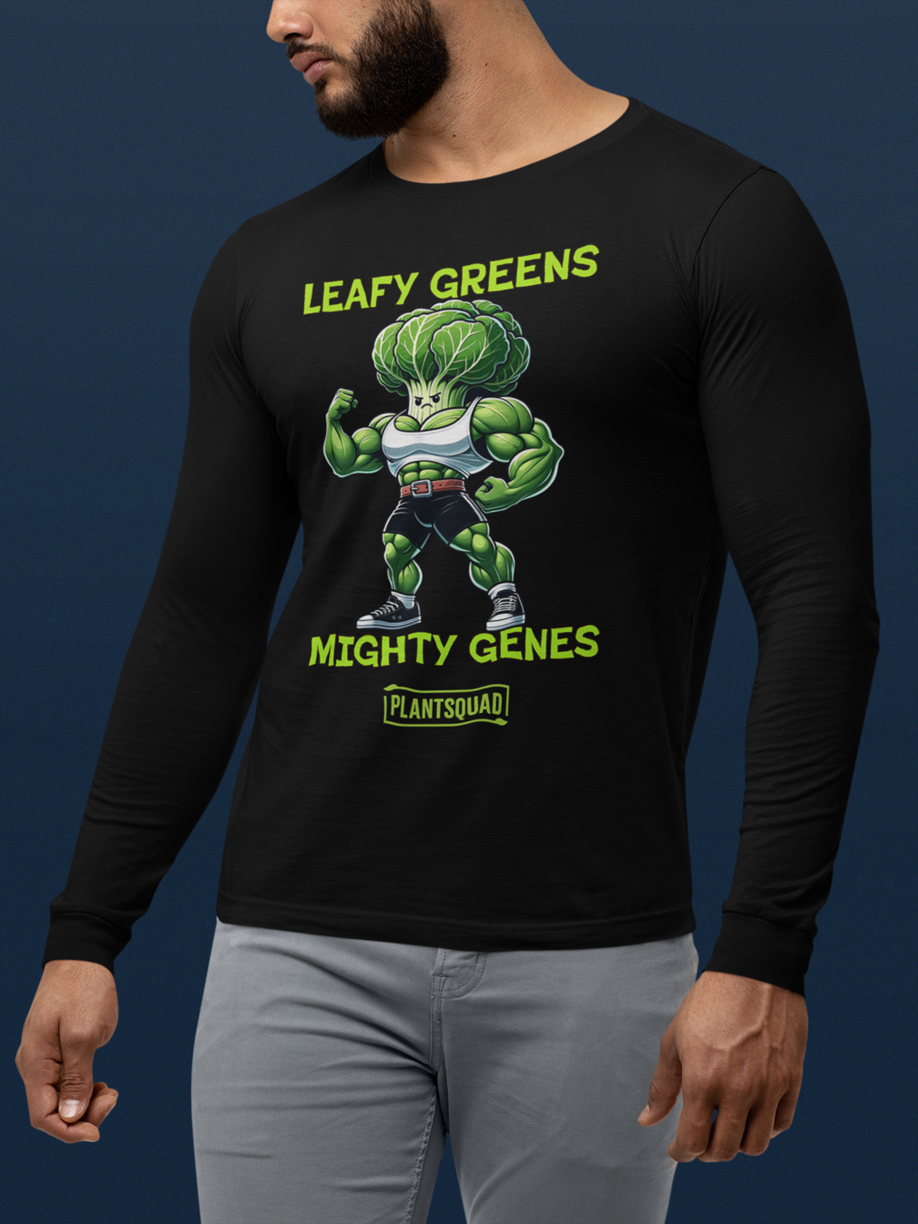 A Plantsquad Cabbage "Leafy Greens Mighty Genes" - Unisex Long Sleeve T-Shirt featuring a muscular cartoon broccoli flexing its arms, perfect for fitness enthusiasts. The broccoli, donning a white tank top and blue shorts, proudly sits under the text "LEAFY GREENS," with "MIGHTY GENES" below. At the bottom is the logo "PLANTSQUAD.