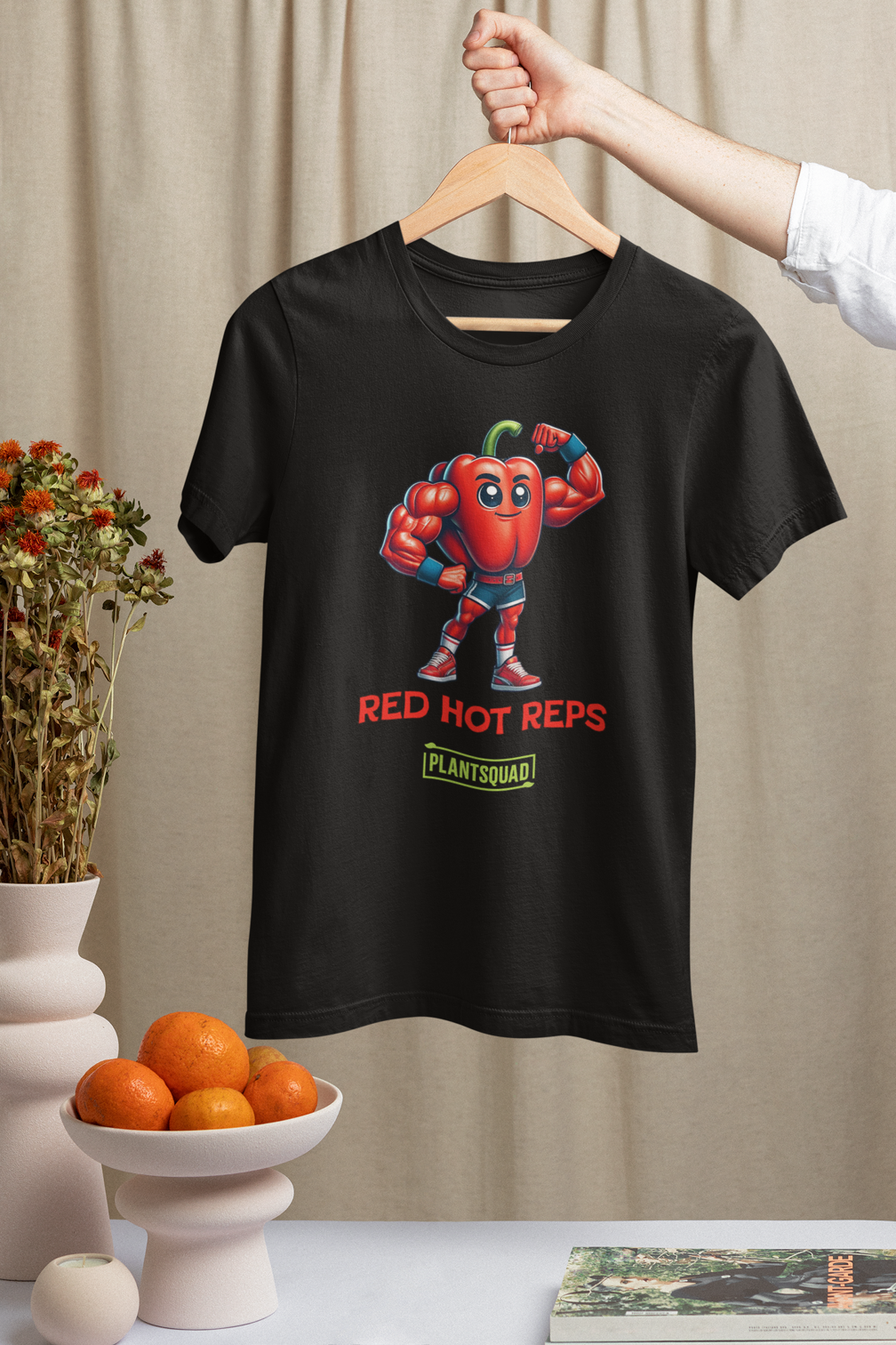 A Plantsquad Capsicum "Red Hot Reps" - Unisex T-Shirt featuring an illustration of a muscular red pepper character flexing its arms. Below the character are the words "RED HOT REPS" in bold red letters, and "PLANTSQUAD" in vibrant green text with a yellow border, showcasing your love for fitness and plant power.