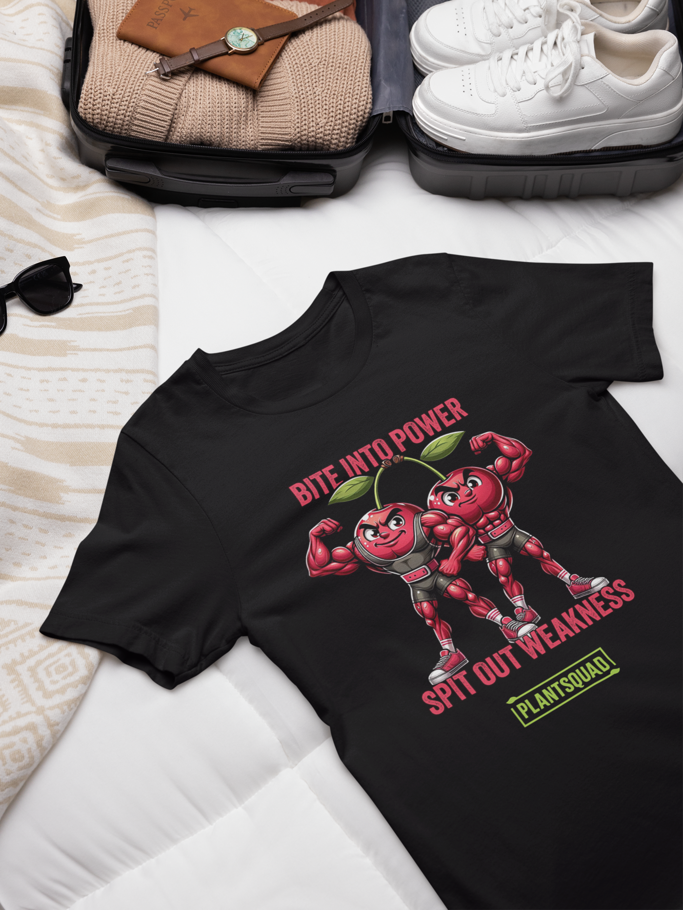 A black Plantsquad Cherries "Bite Into Power Spit Out Weakness" - Unisex T-shirt features two muscular cartoon cherries flexing their arms. Above them, pink text reads "Bite Into Power." Below them, white text reads "Spit Out Weakness." At the bottom, there's a green and yellow Plantsquad logo.