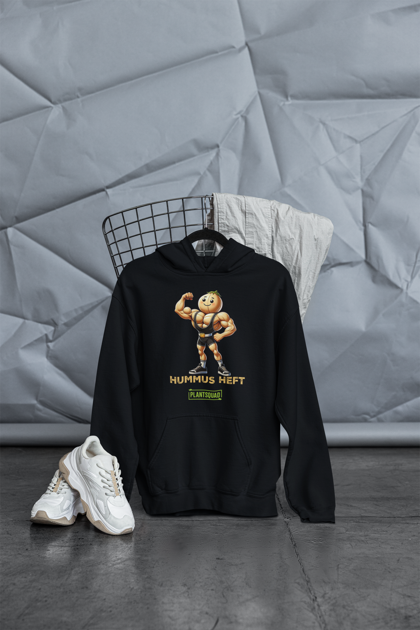 The Plantsquad Chickpea "Hummus Heft" - Unisex Hoodie features a black hooded sweatshirt with a cartoon hummus mascot flexing its biceps, embodying the weight-lifting chickpea spirit. The text "Hummus Heft" is printed below the character, with "PLANTSQUAD" in a green box underneath, perfect for showcasing your vegan lifestyle.