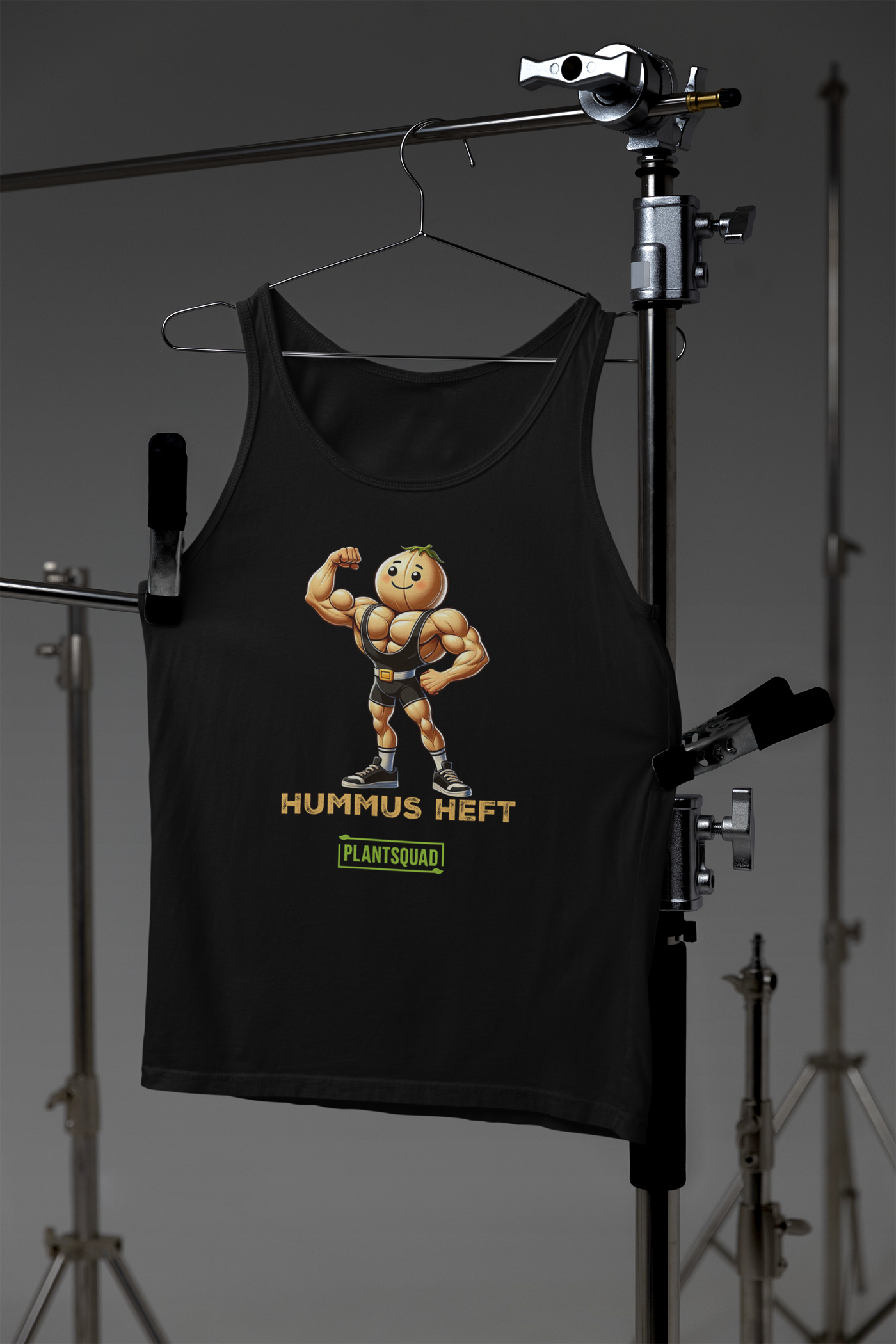 A black tank top made from breathable fabric, featuring an illustration of a muscular chickpea character flexing its arm, with the text "Hummus Heft" and a small green label reading "PlantSquad," perfect for a vegan workout tank top that celebrates the plant-based lifestyle can be replaced with Plantsquad Chickpea "Hummus Heft" - Unisex Tank Top.