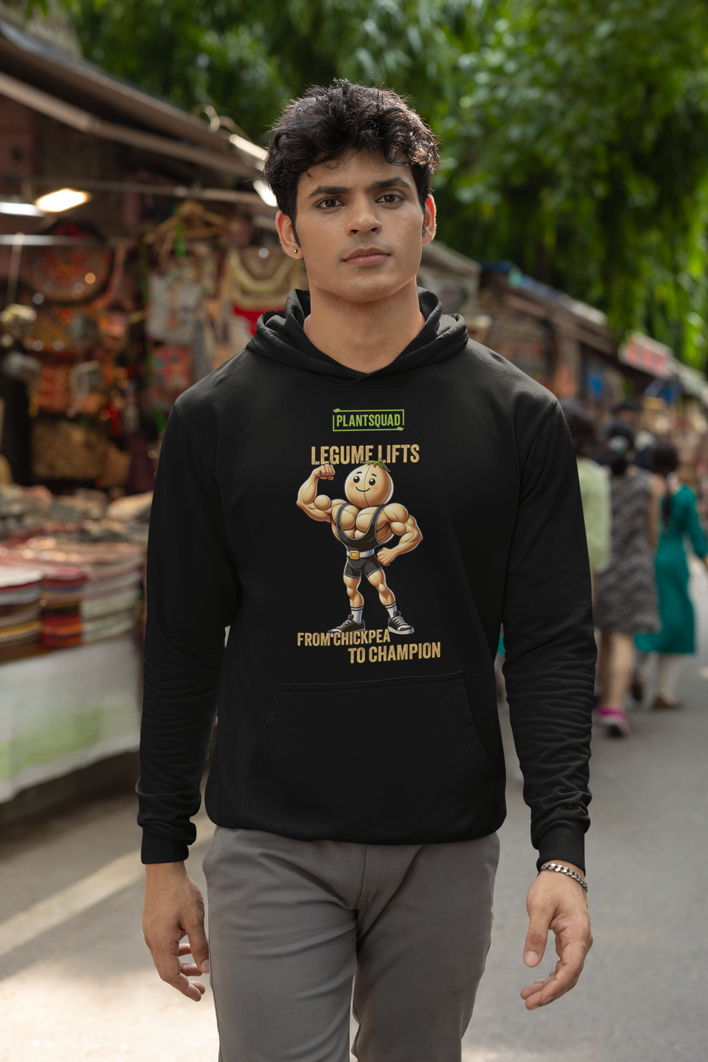 A black Plantsquad Chickpea "Legume Lifts" - Unisex Hoodie features a muscular chickpea cartoon character lifting a dumbbell. Above the character, text reads "Plantsquad" and "Legume Lifts." Below, it says "From Chickpea to Champion." The design is centered on the chest area of the hoodie, perfect for showing off your vegan lifestyle.