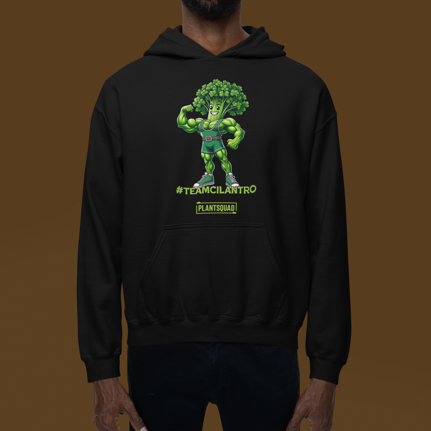 The Plantsquad Cilantro "Team Cilantro" - Unisex Hoodie features a cartoon of a muscular, flexing cilantro superhero, perfect for those embracing a vegan lifestyle. The character has a leafy head, an eye mask, and a belt. Below the character, the text reads "#TEAMCILANTRO" and "PLANTSQUAD.